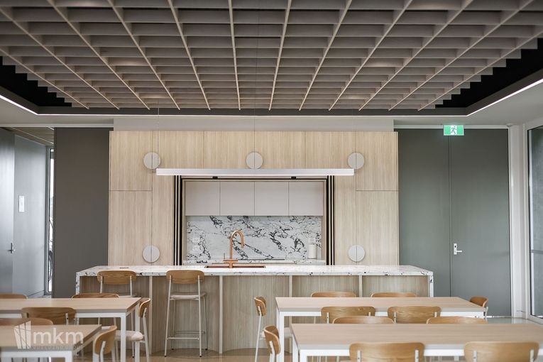 Interior view of a modern kitchen with a grid ceiling, marble backsplash, and tables with chairs.