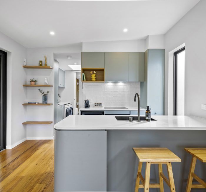 Modern kitchen with grey cabinets, white countertops, and wooden stools.