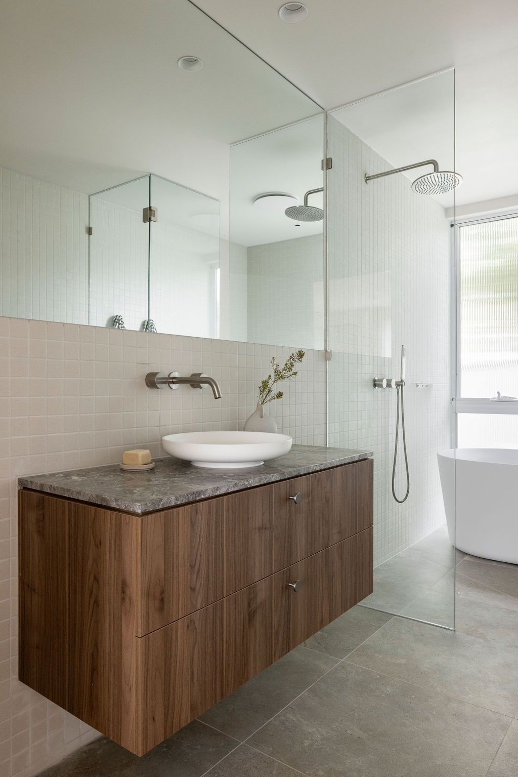 Modern bathroom with floating wooden vanity, white vessel sink, large mirror, and glass shower enclosure.