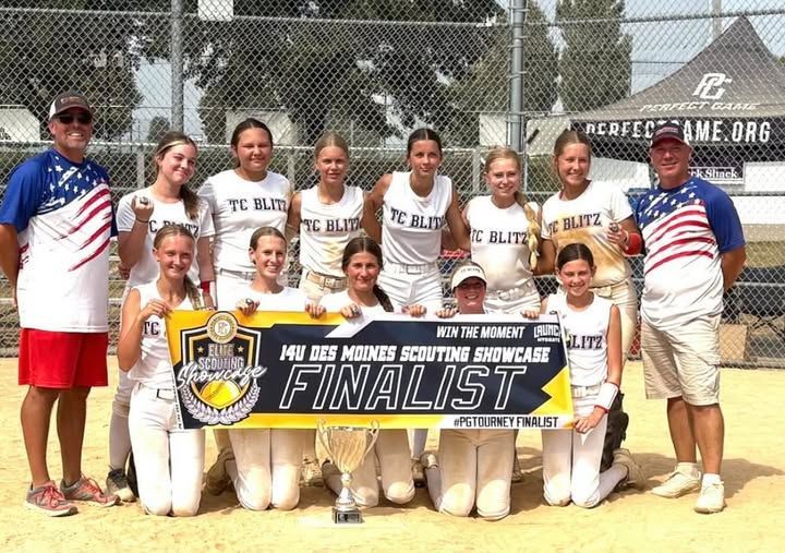 Youth softball team posing with medals on a dirt field, coaches standing behind them.