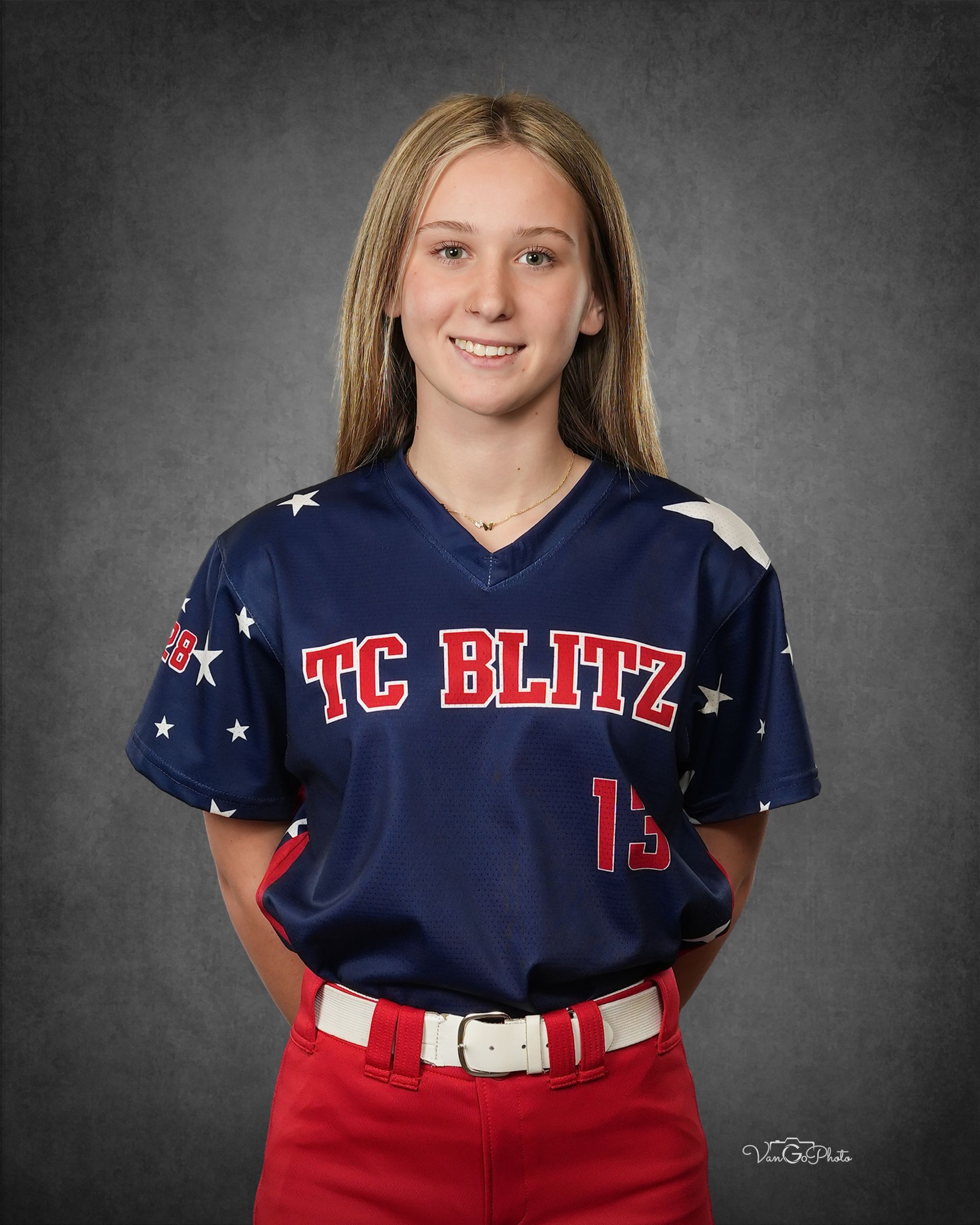 Portrait of a smiling softball player in navy TC BLITZ jersey and red pants against a gray backdrop