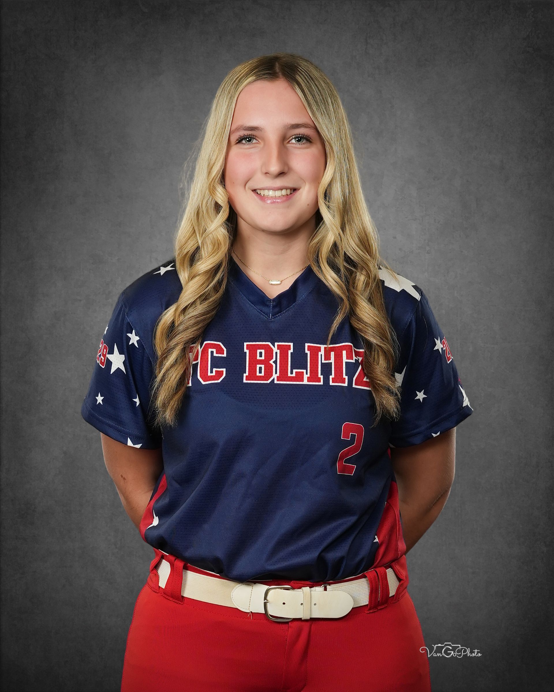 Portrait of a softball player in a navy and red uniform, smiling against a gray studio backdrop.