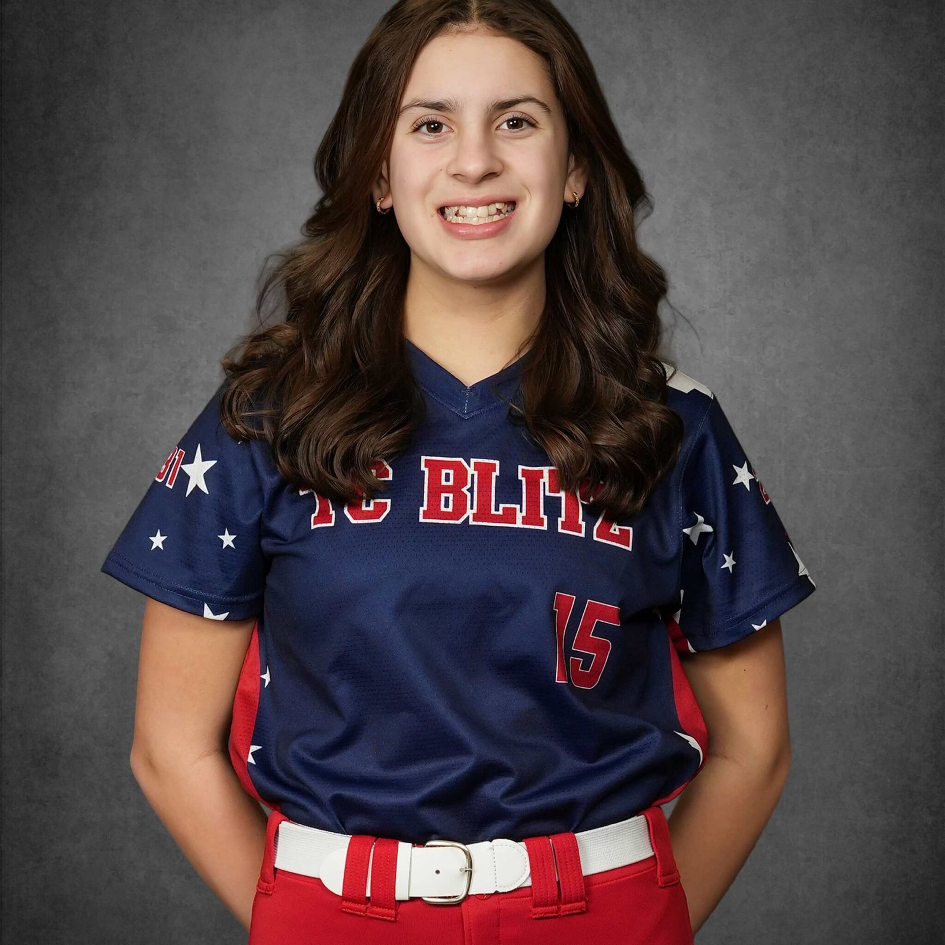 Smiling softball player in navy jersey and red pants, standing against a gray backdrop.