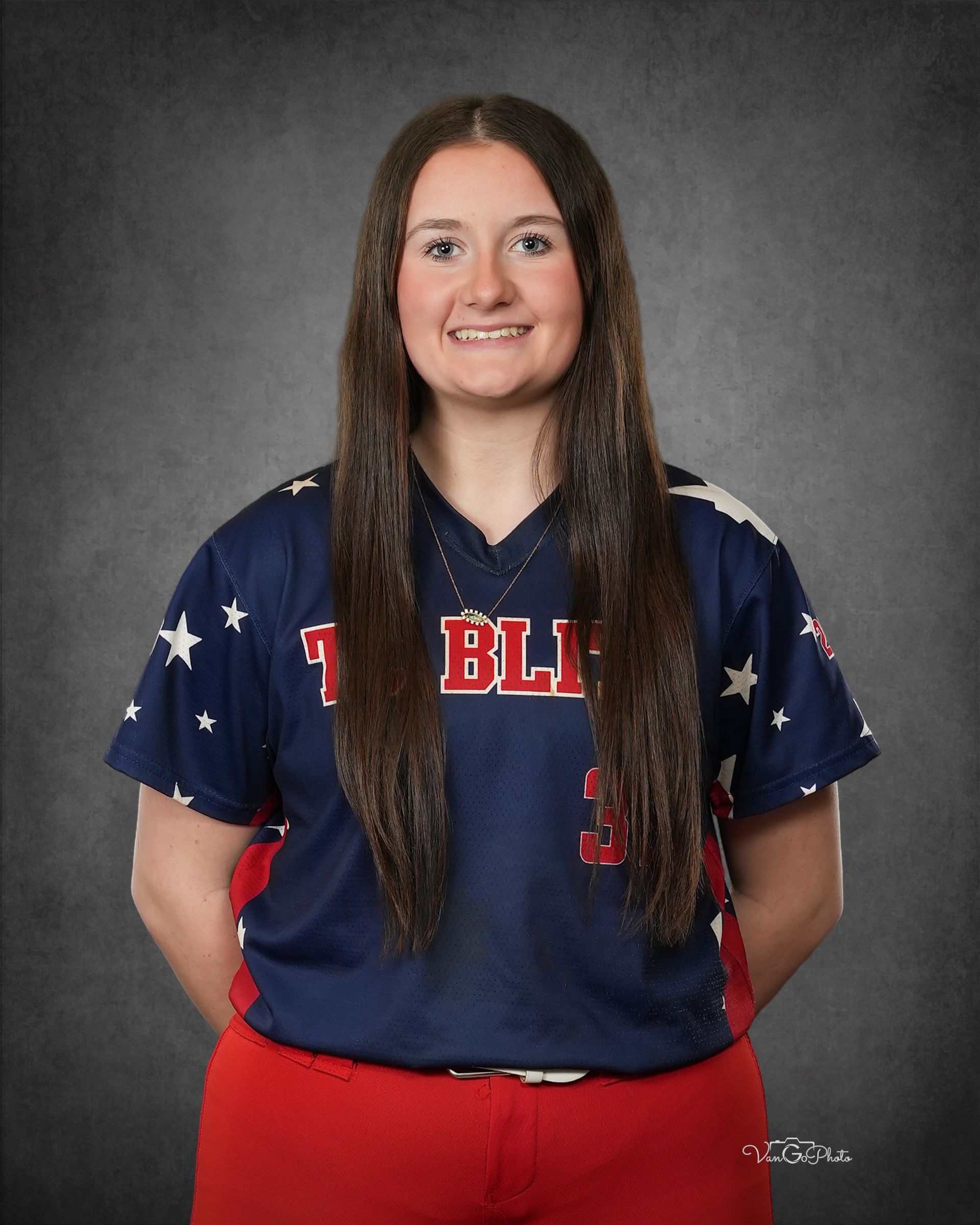 Smiling athlete in navy and red softball uniform against a gray studio backdrop.