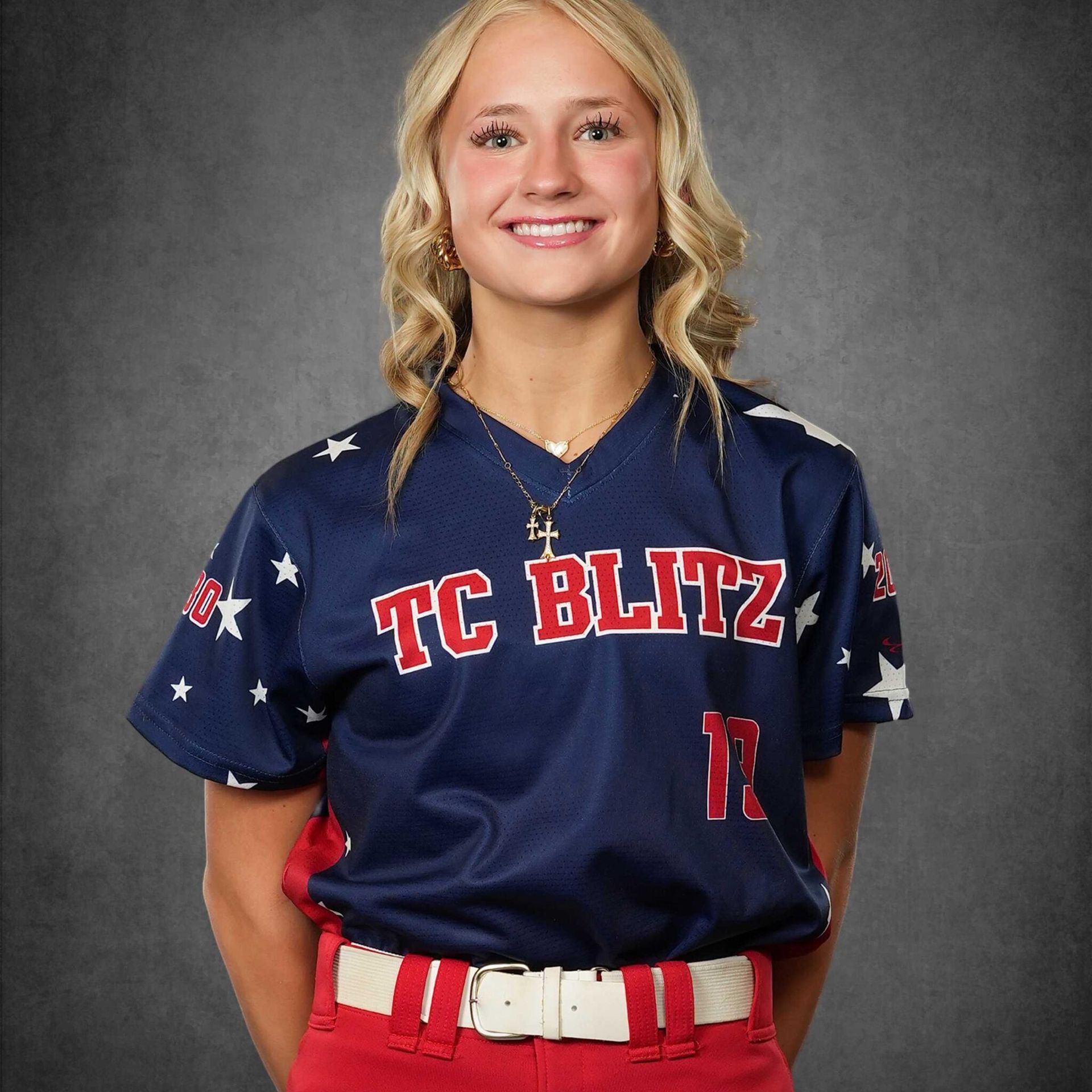 Smiling softball player in navy and red TC BLITZ uniform against a gray backdrop