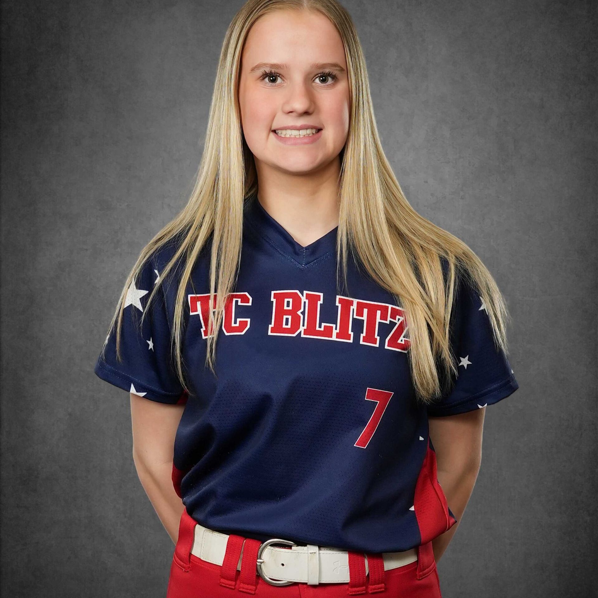 Youth baseball player in navy and red TC Blitz jersey, standing against a gray studio backdrop.