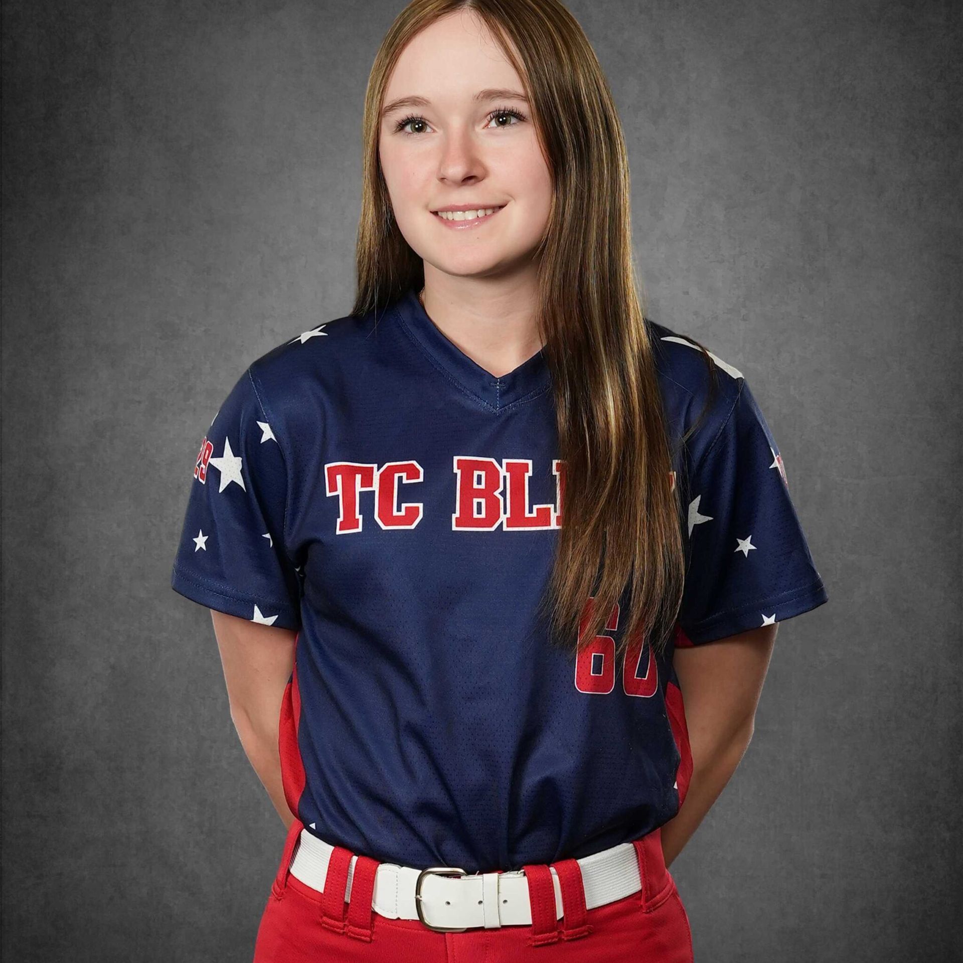 Portrait of a softball player in a navy and red uniform standing against a gray backdrop