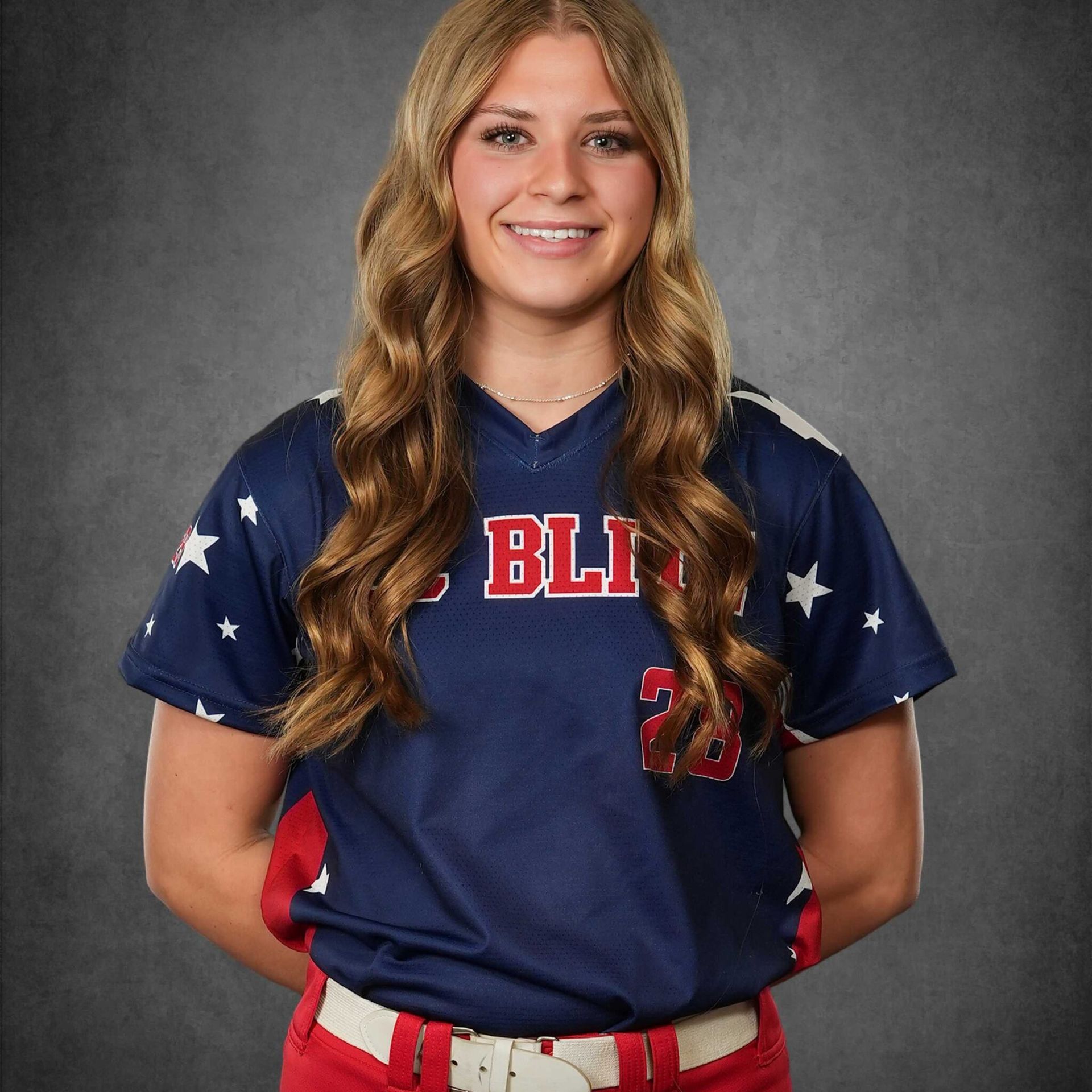 Female softball player in navy and red uniform smiling against a gray studio backdrop