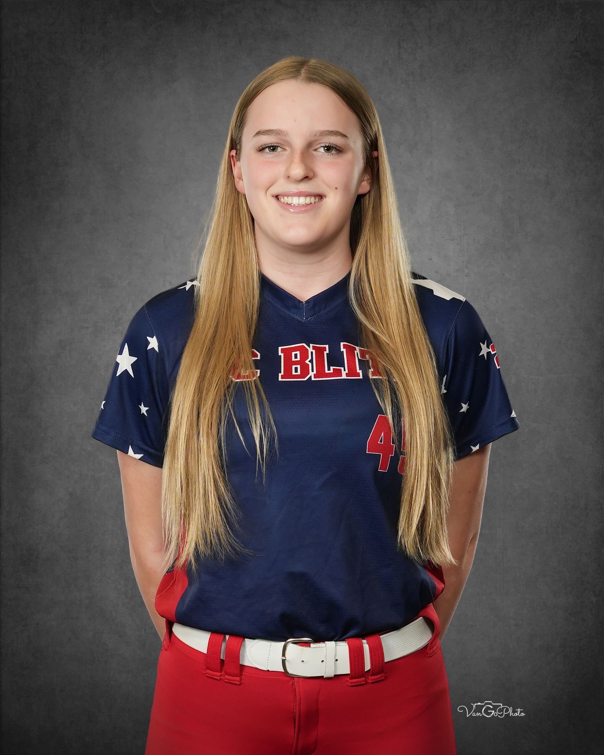 Portrait of a person in a navy and red sports uniform standing against a gray studio backdrop, smiling.