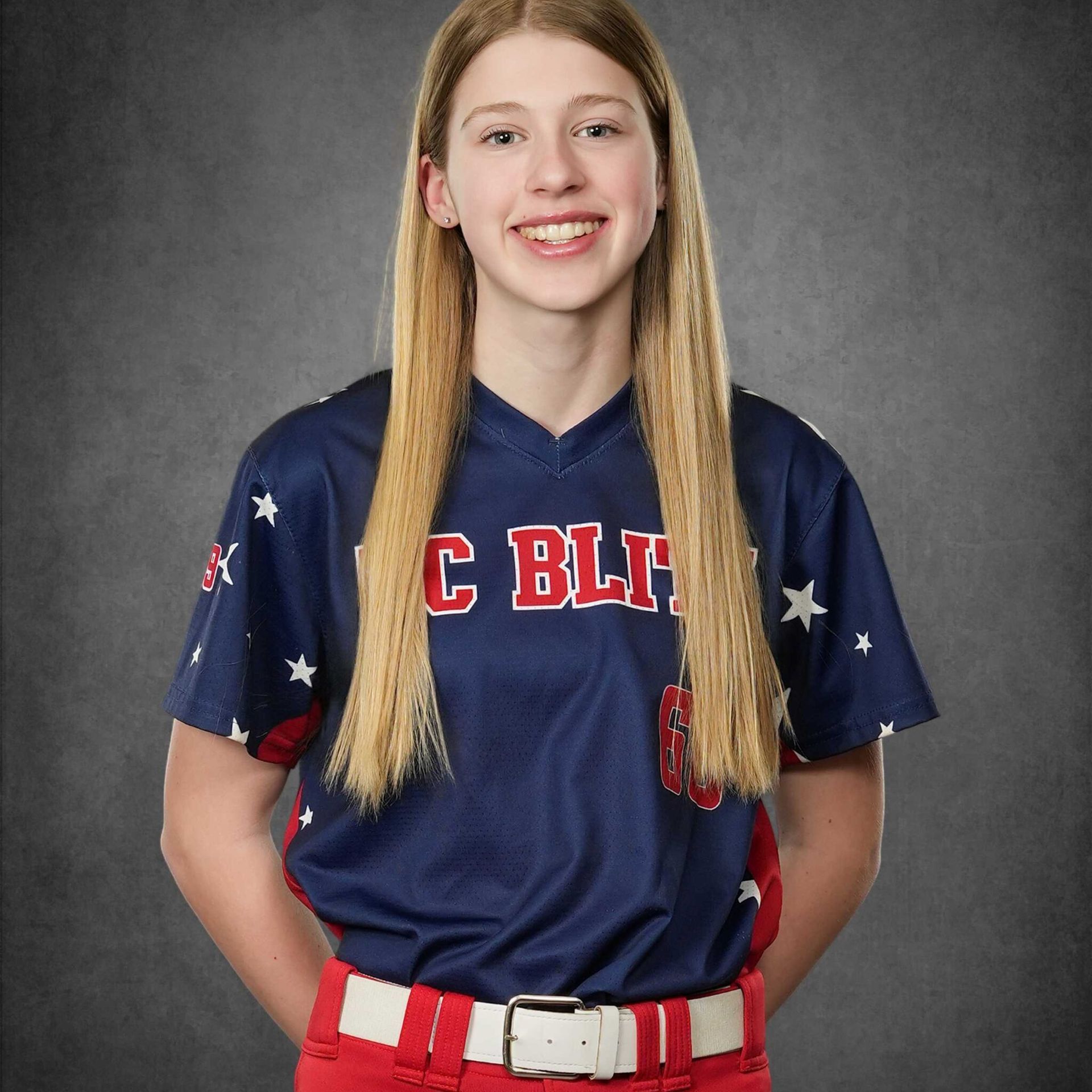 Smiling softball player in navy and red uniform against a gray studio backdrop