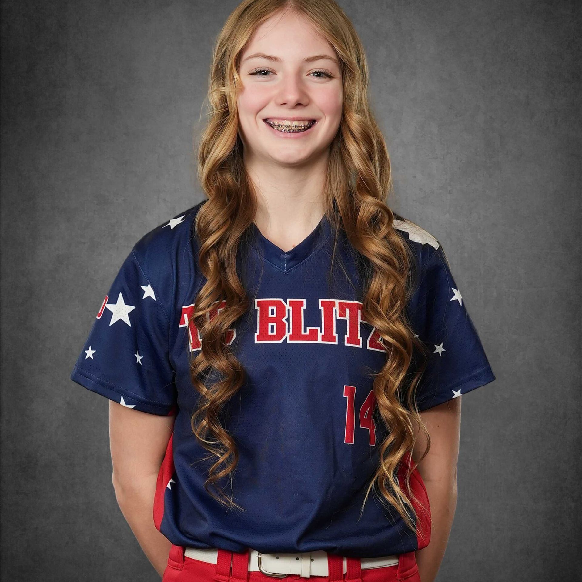 Smiling softball player in navy red-and-white jersey against a gray studio backdrop