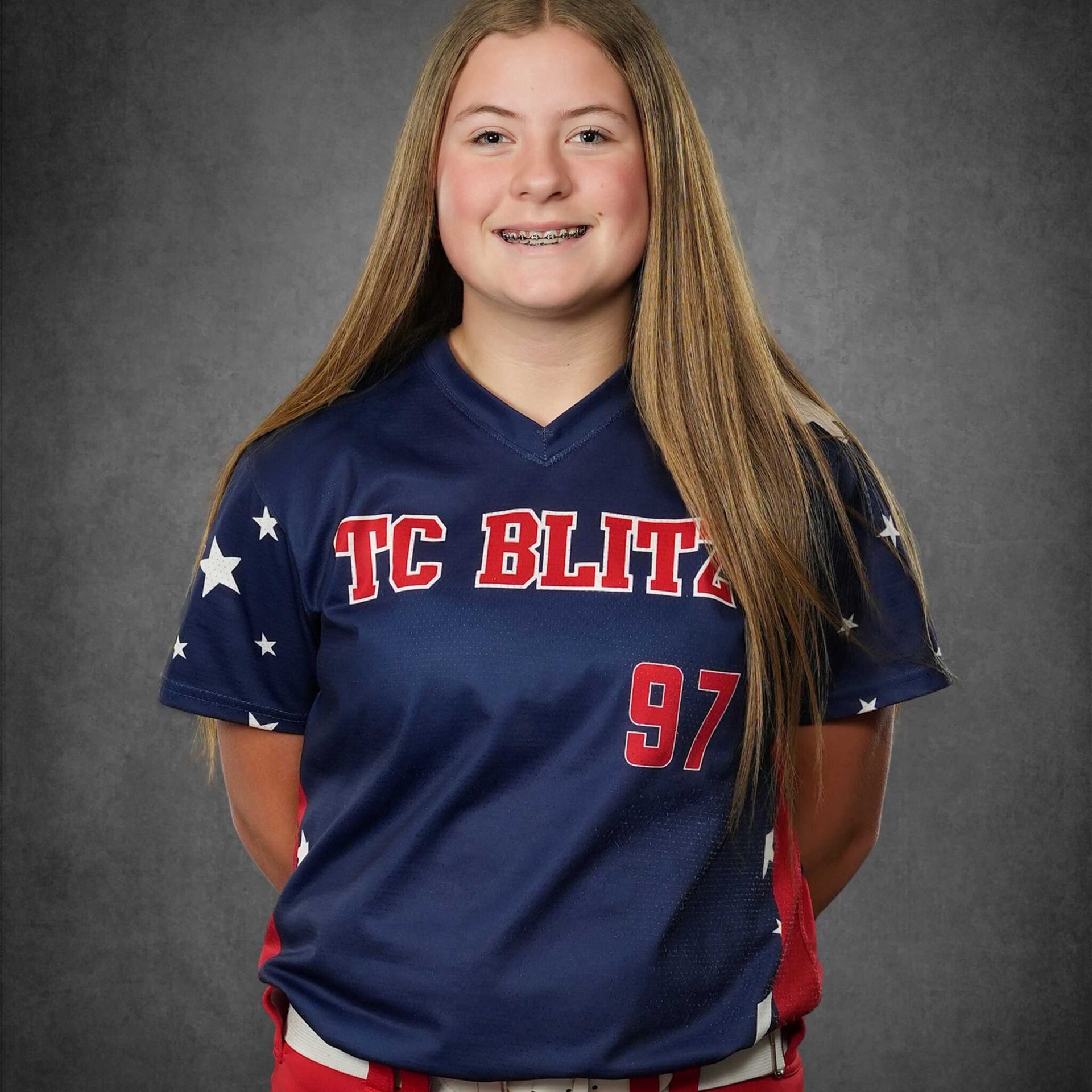 Softball player in navy jersey with red accents and number 97, standing against a gray backdrop.