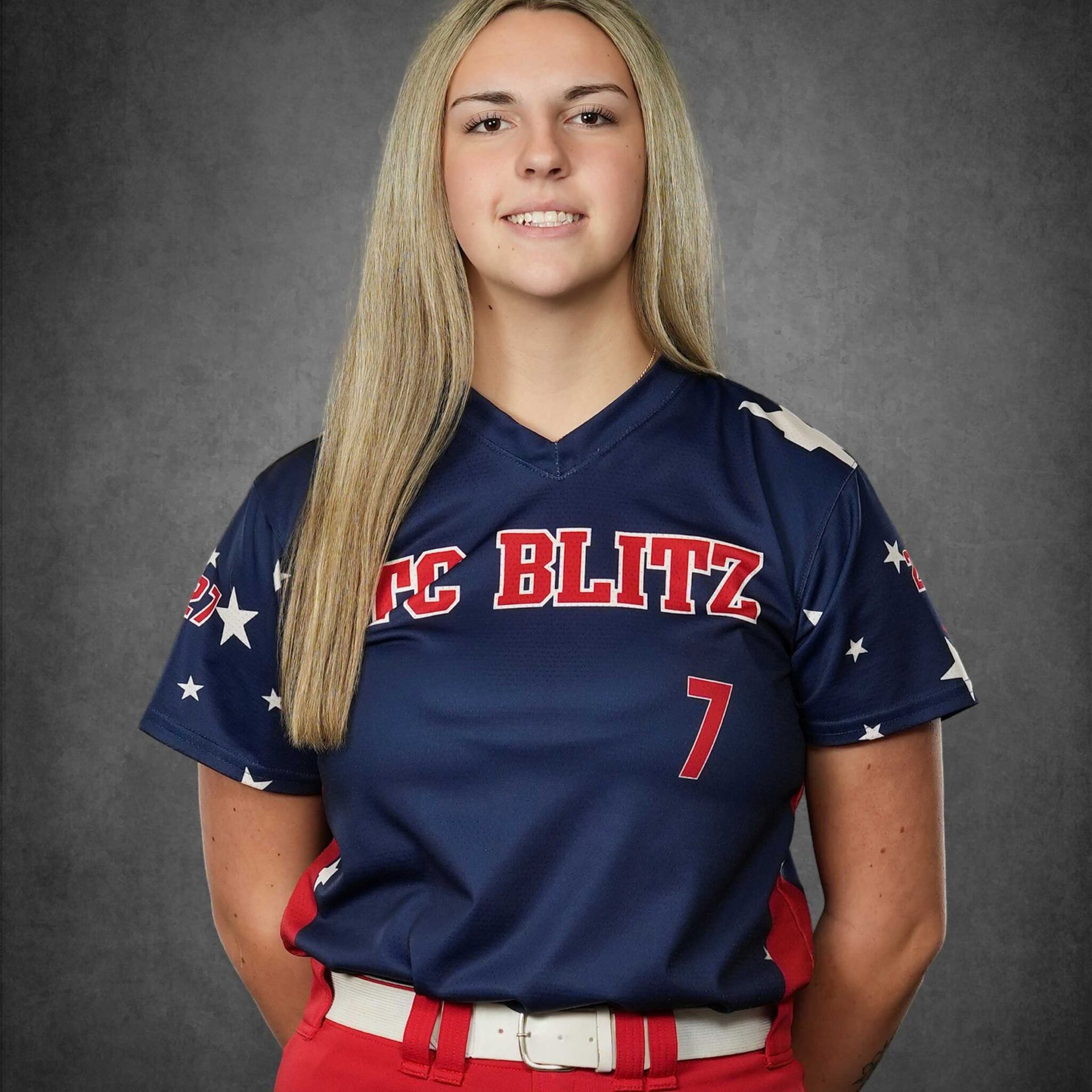 Softball player in navy jersey and red belt posing against a gray studio backdrop