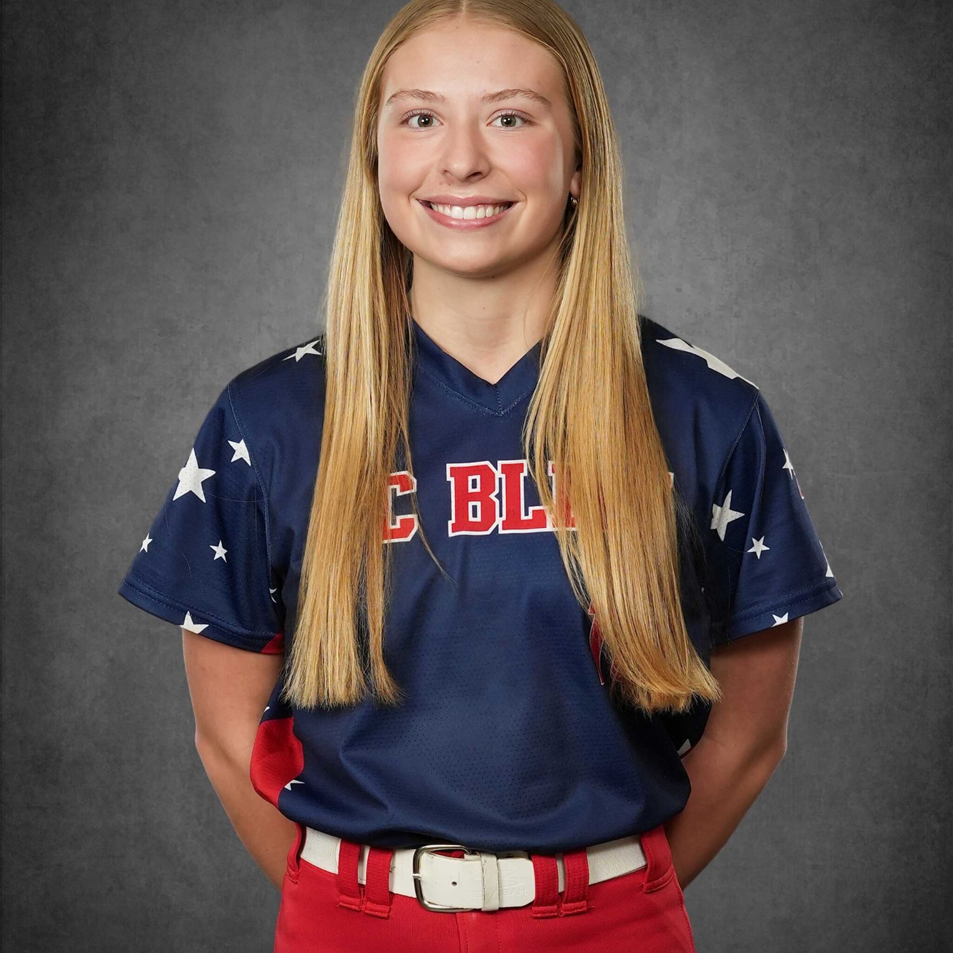 Smiling softball player in navy and red uniform against a gray studio backdrop