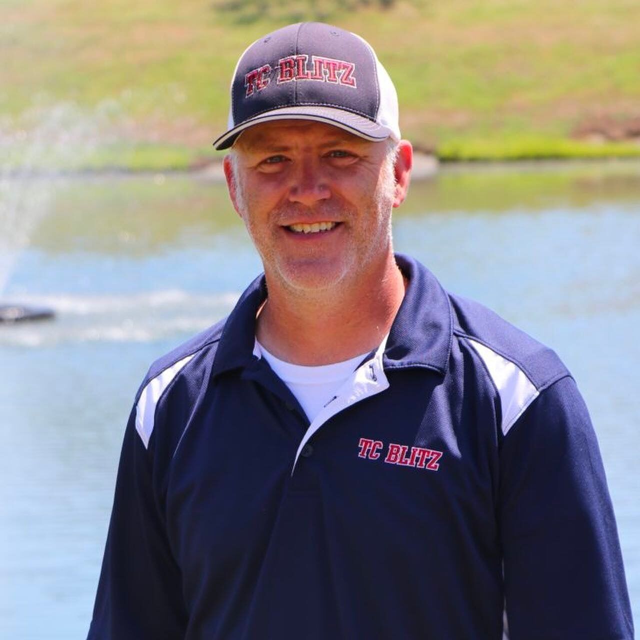 Man in a navy shirt and cap smiling outdoors near water