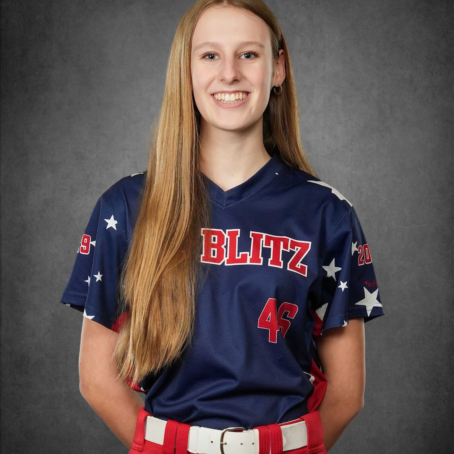 Portrait of a softball player in a navy BLITZ jersey, smiling against a gray studio backdrop