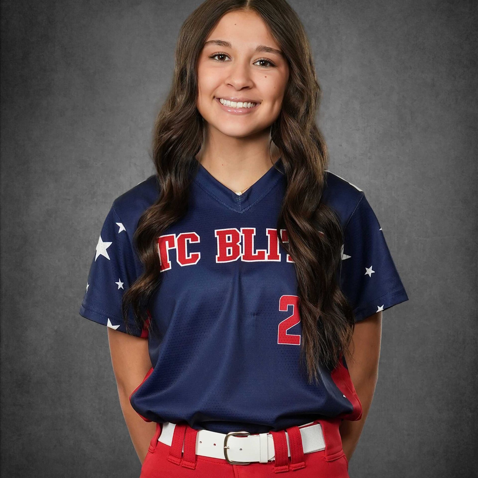 Smiling softball player in navy and red uniform standing against a gray backdrop