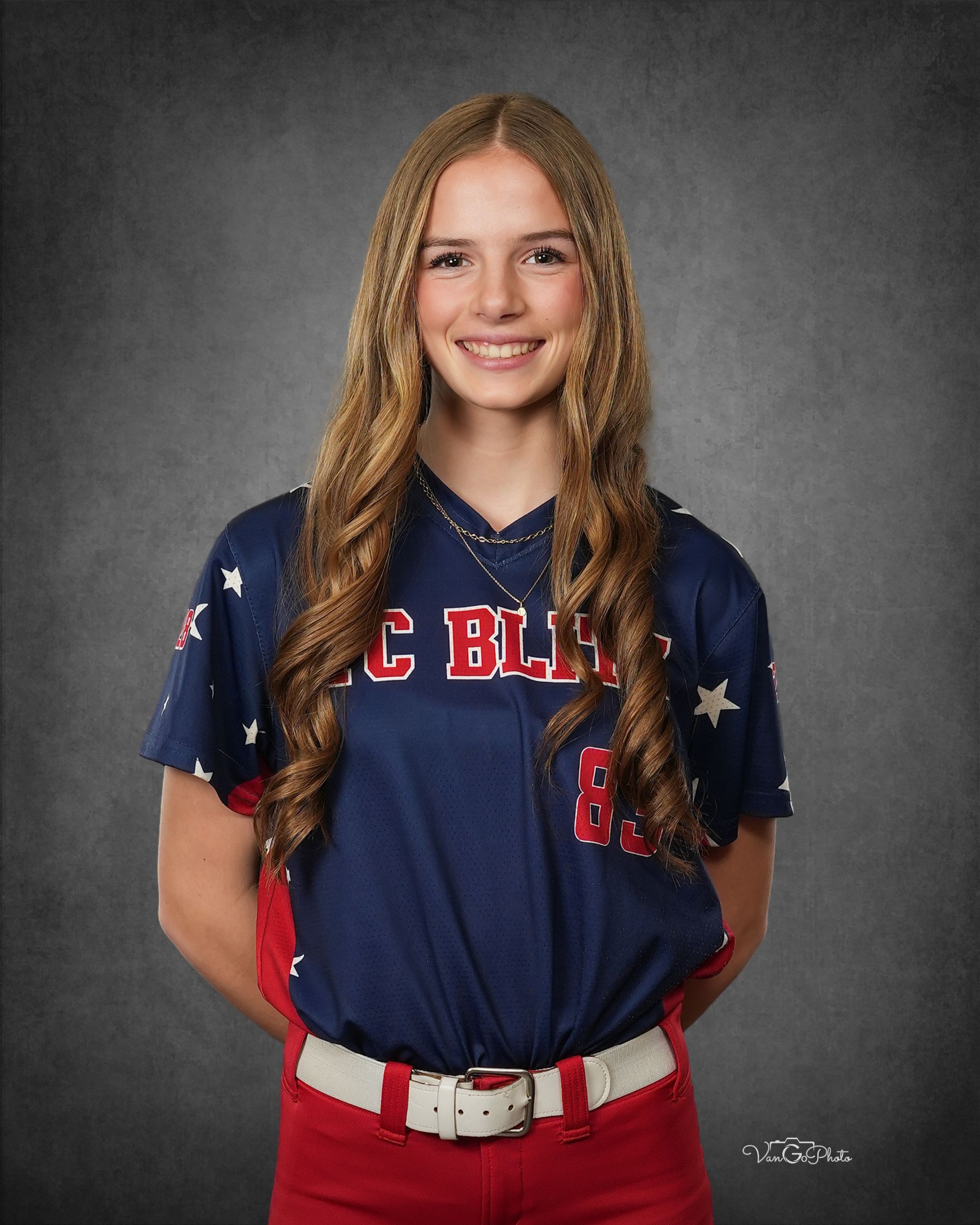 Portrait of a smiling student in a navy and red baseball uniform against a gray backdrop