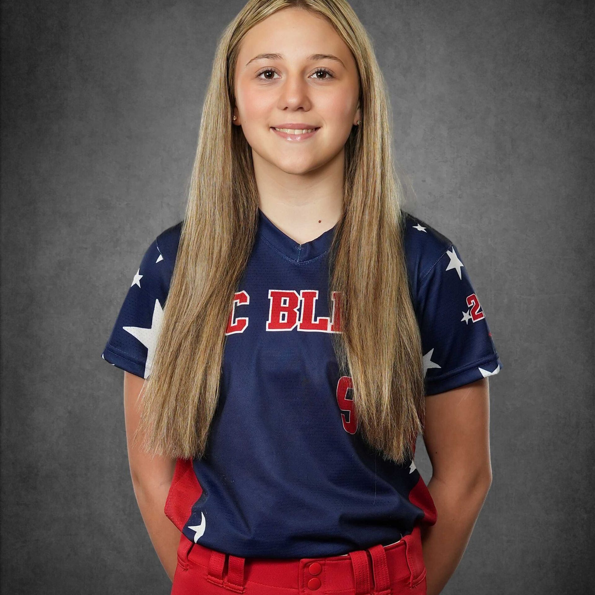 Portrait of a smiling student athlete in a navy and red jersey against a gray studio backdrop
