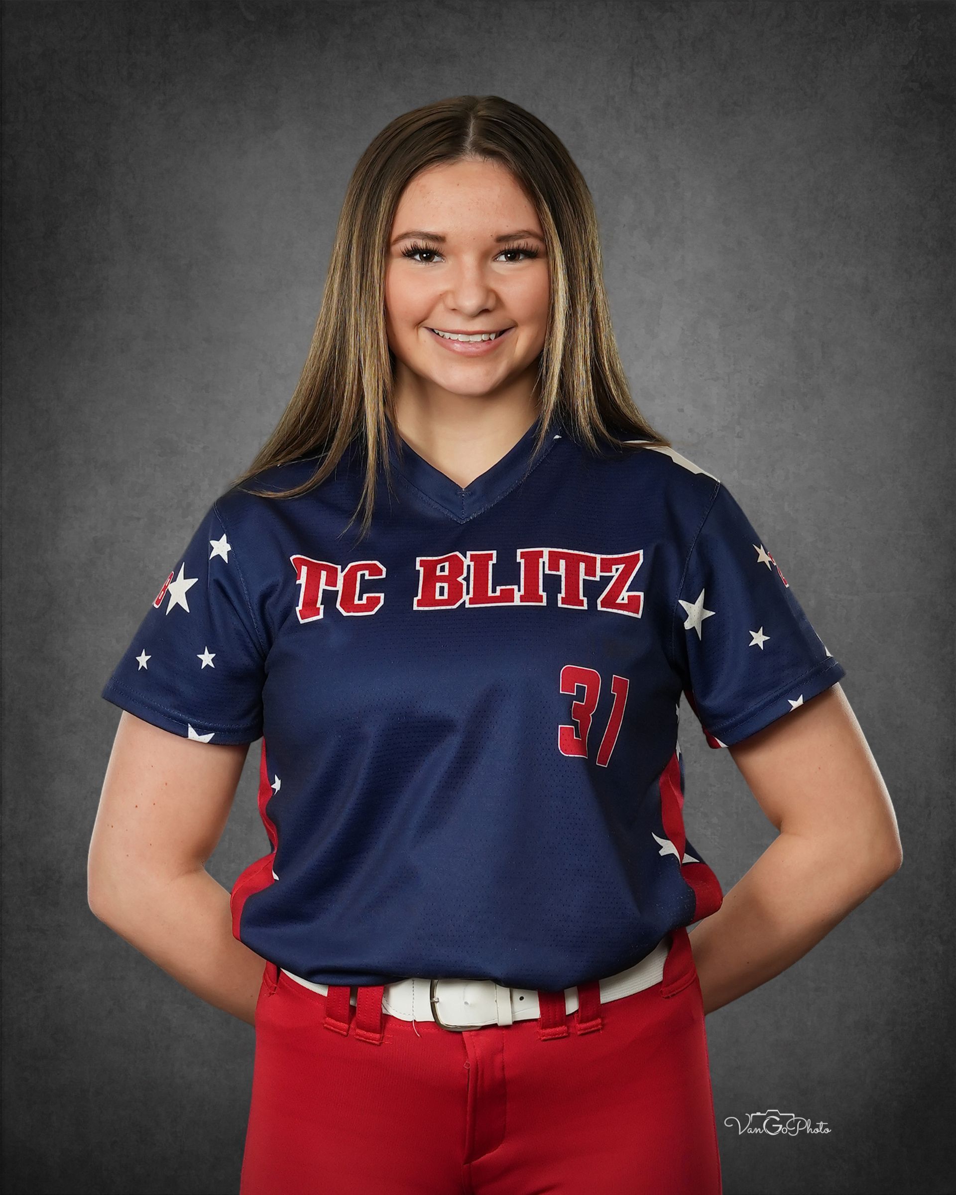 Young athlete in navy and red softball uniform posing against a gray studio backdrop