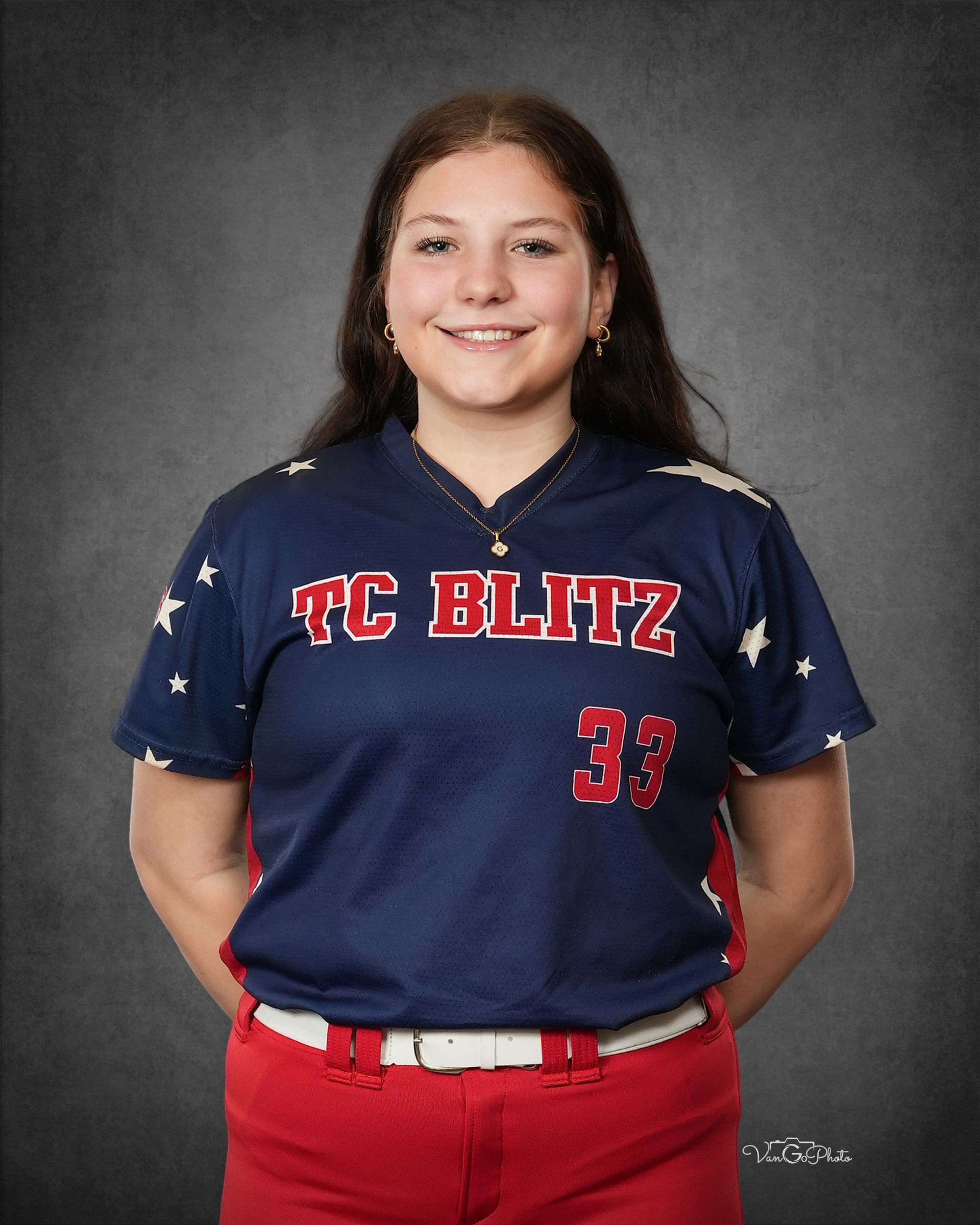 Portrait of a smiling softball player in a navy TC BLITZ jersey and red pants against a gray backdrop