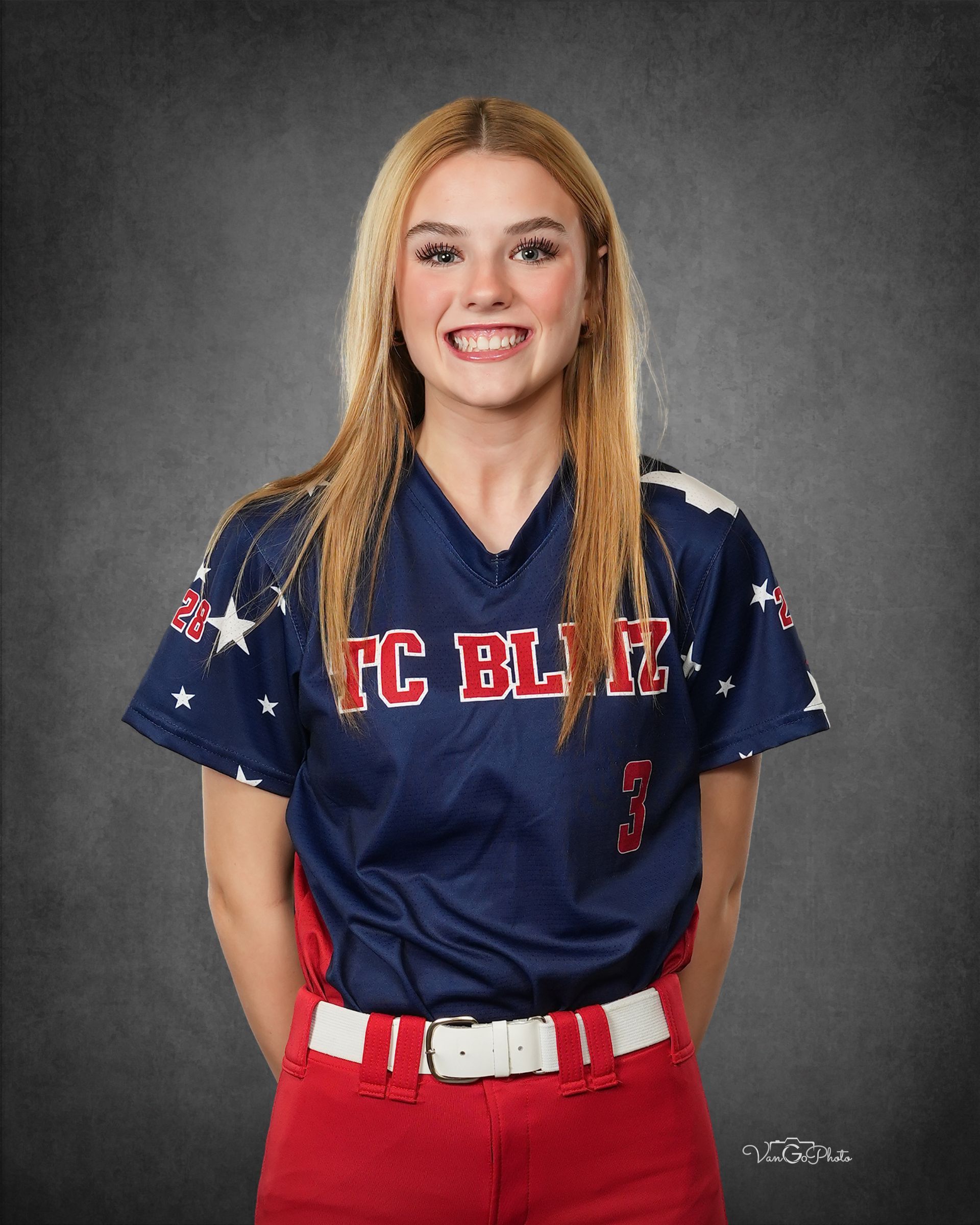 Portrait of a smiling softball player in a navy jersey and red pants against a gray backdrop