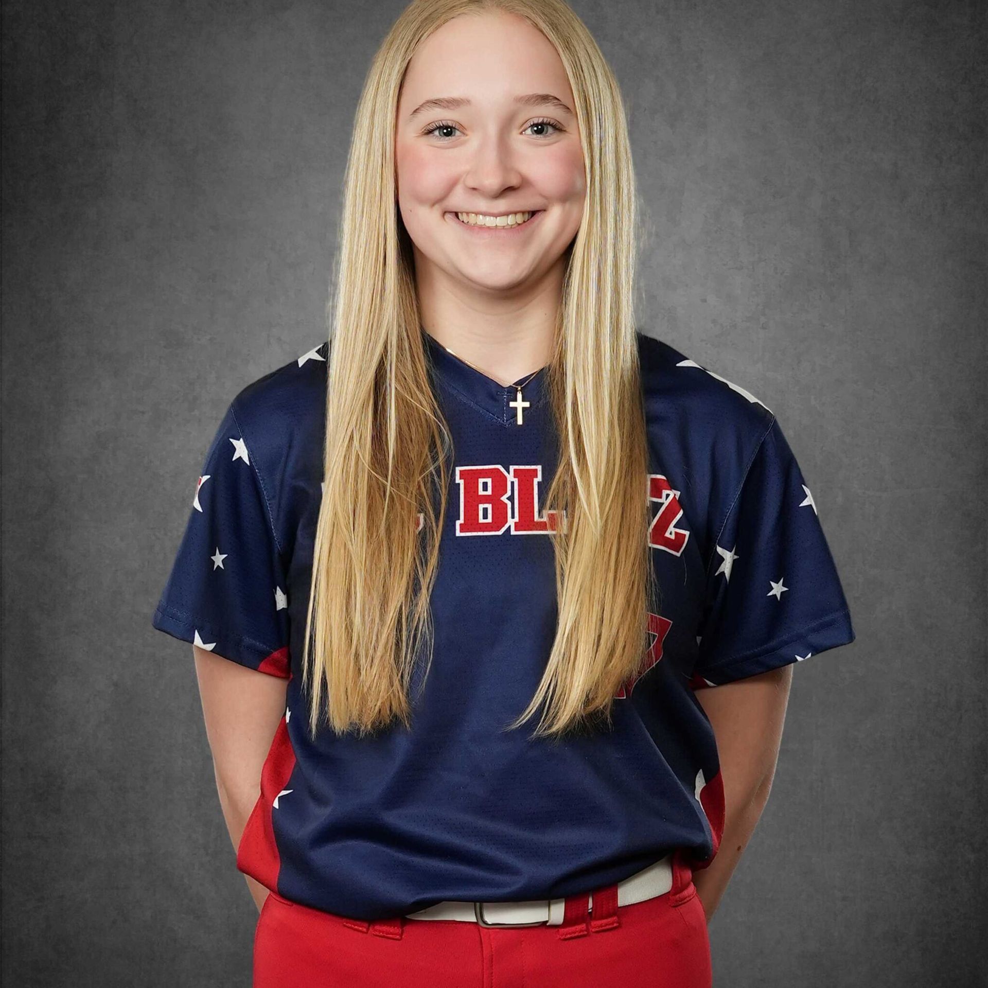 Person in a navy sports shirt and red pants smiling against a gray studio backdrop.