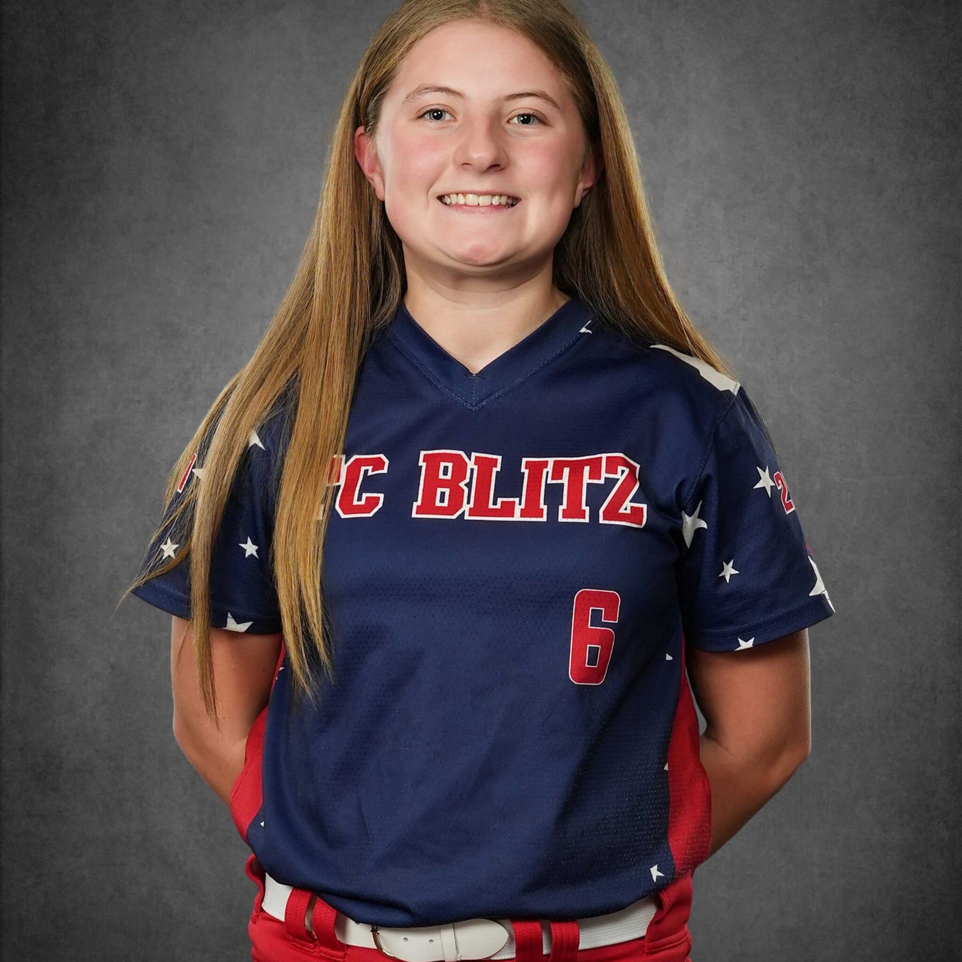 Softball player in navy jersey with red and white accents, smiling against a gray studio backdrop