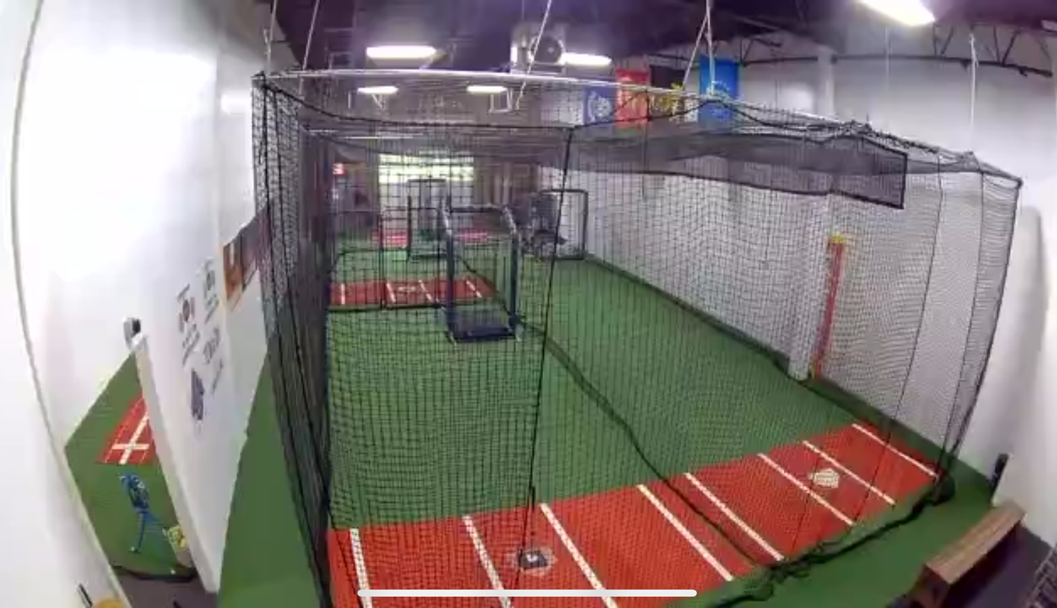 Indoor batting cages with green turf, red platforms, and black netting in a training facility