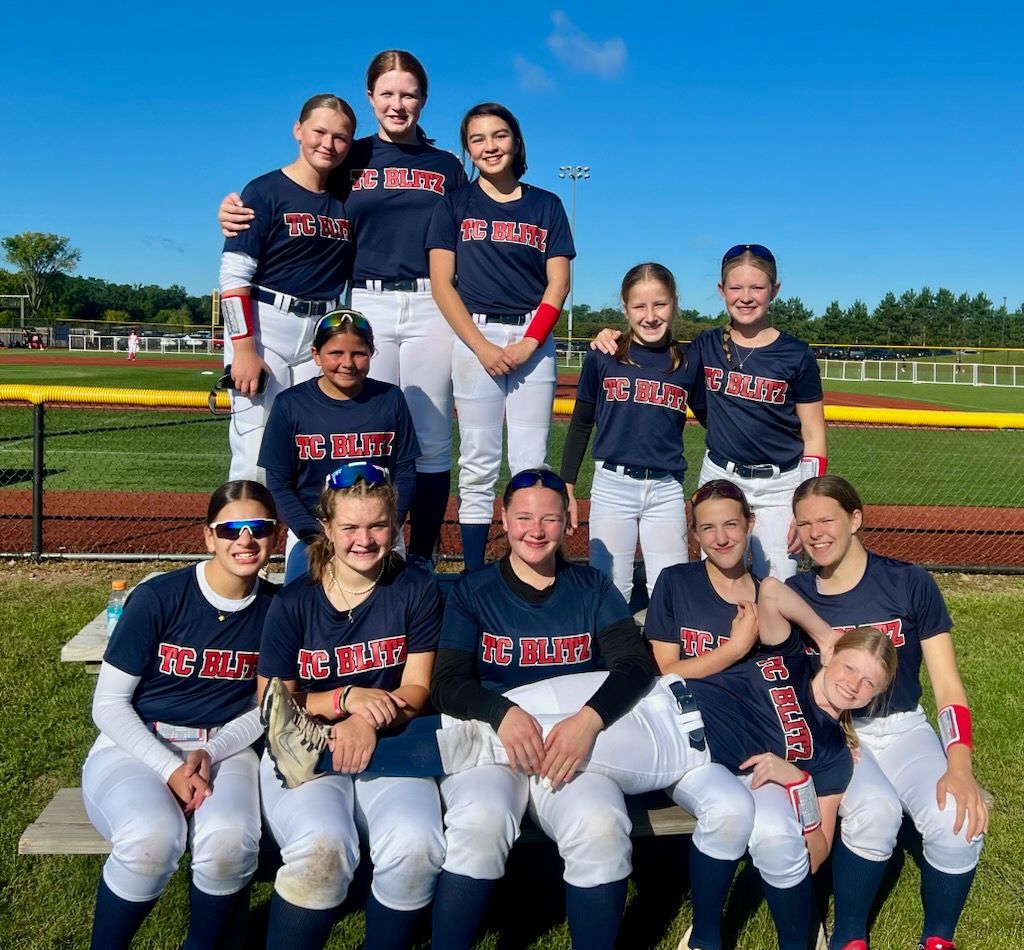 Youth softball team posing in navy uniforms on a field under a bright blue sky
