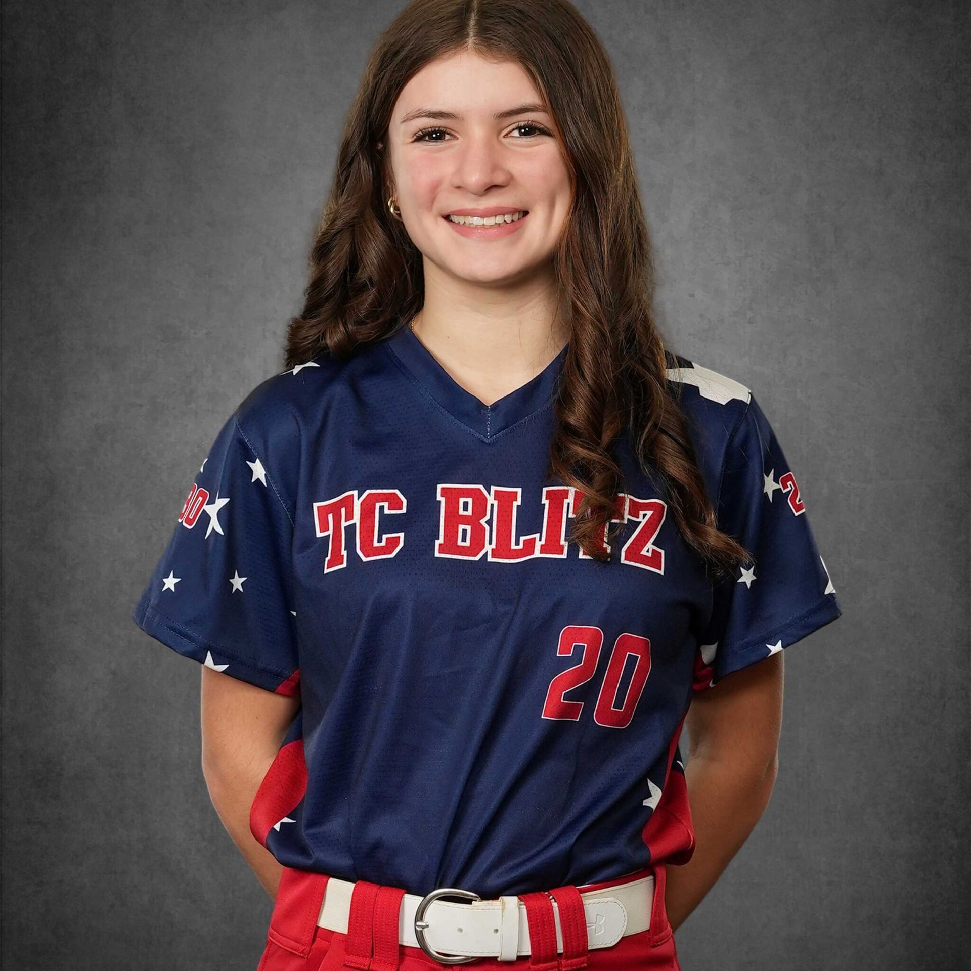 Portrait of a smiling softball player in a navy TC Blitz jersey and red belt, standing against a gray backdrop