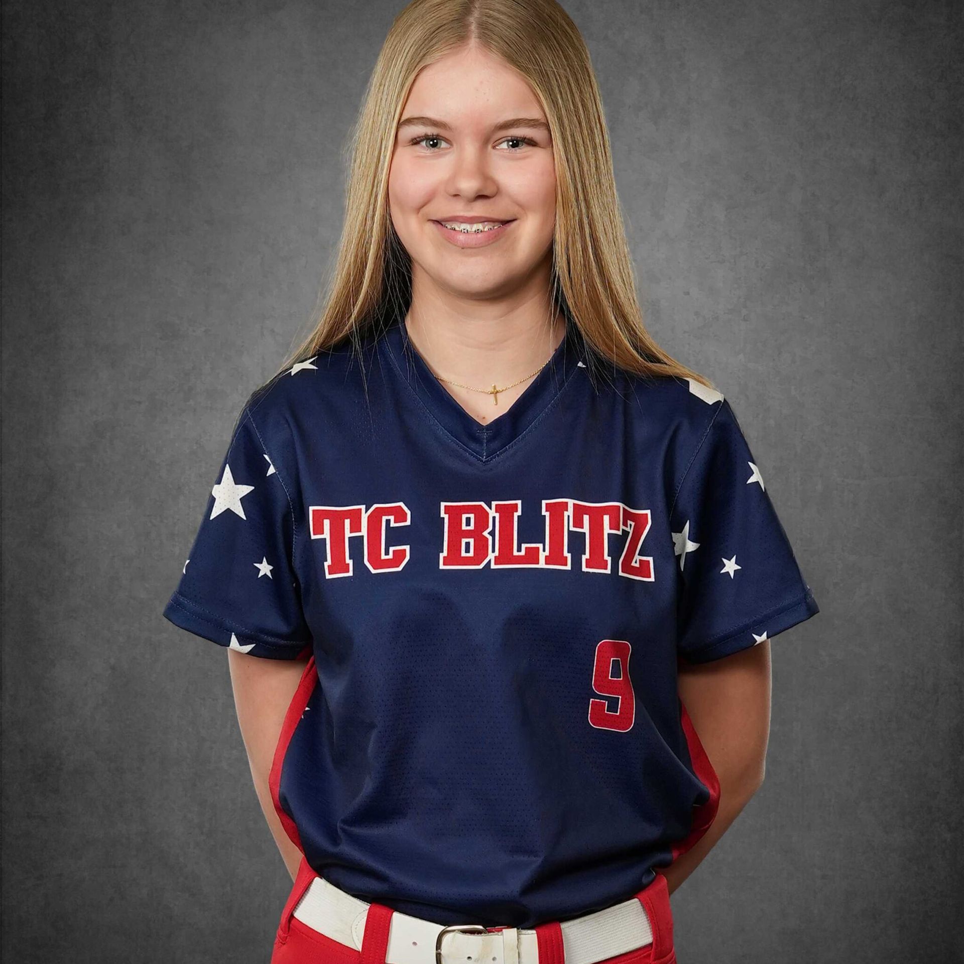 Smiling youth softball player in navy TC Blitz jersey against a gray studio backdrop