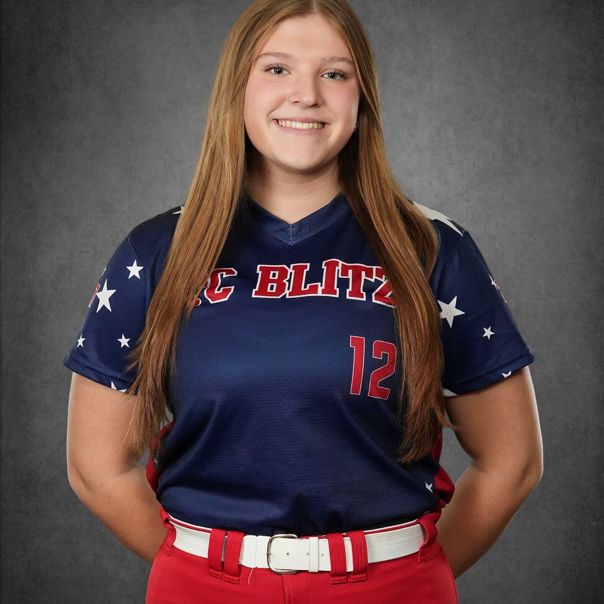 Portrait of a smiling athlete in a navy and red softball jersey, standing against a gray studio backdrop.