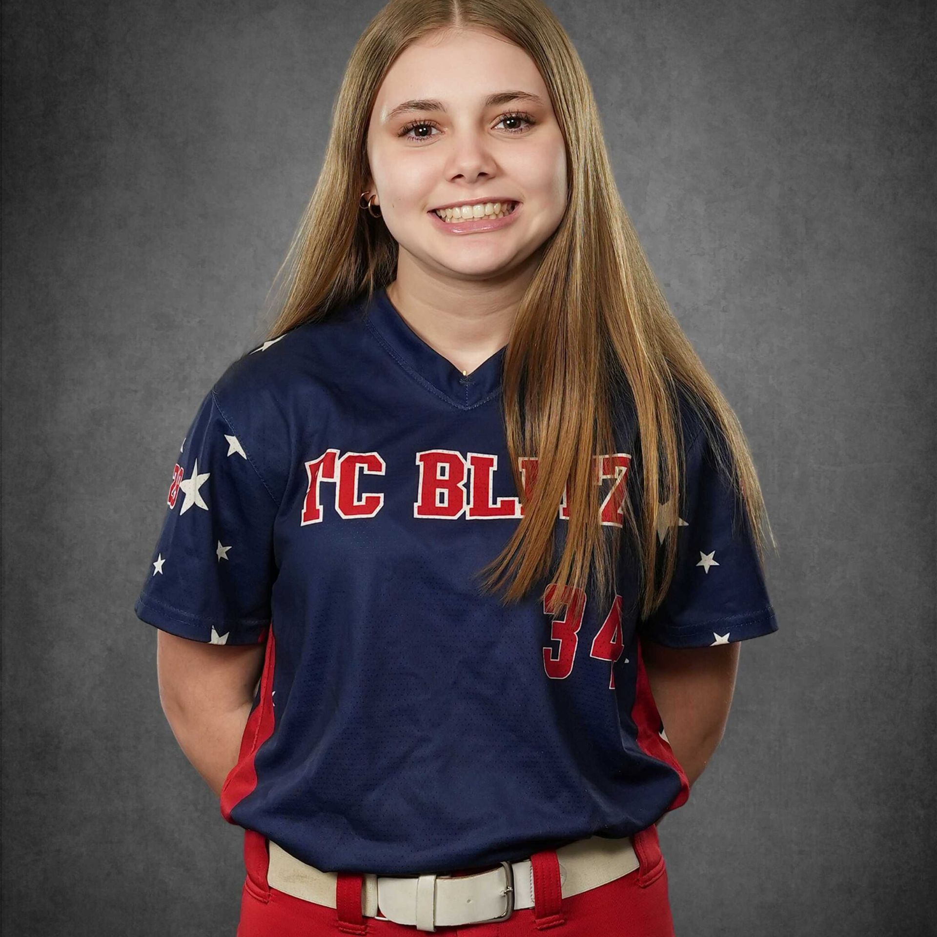 Smiling softball player in navy jersey with red lettering against a gray studio backdrop