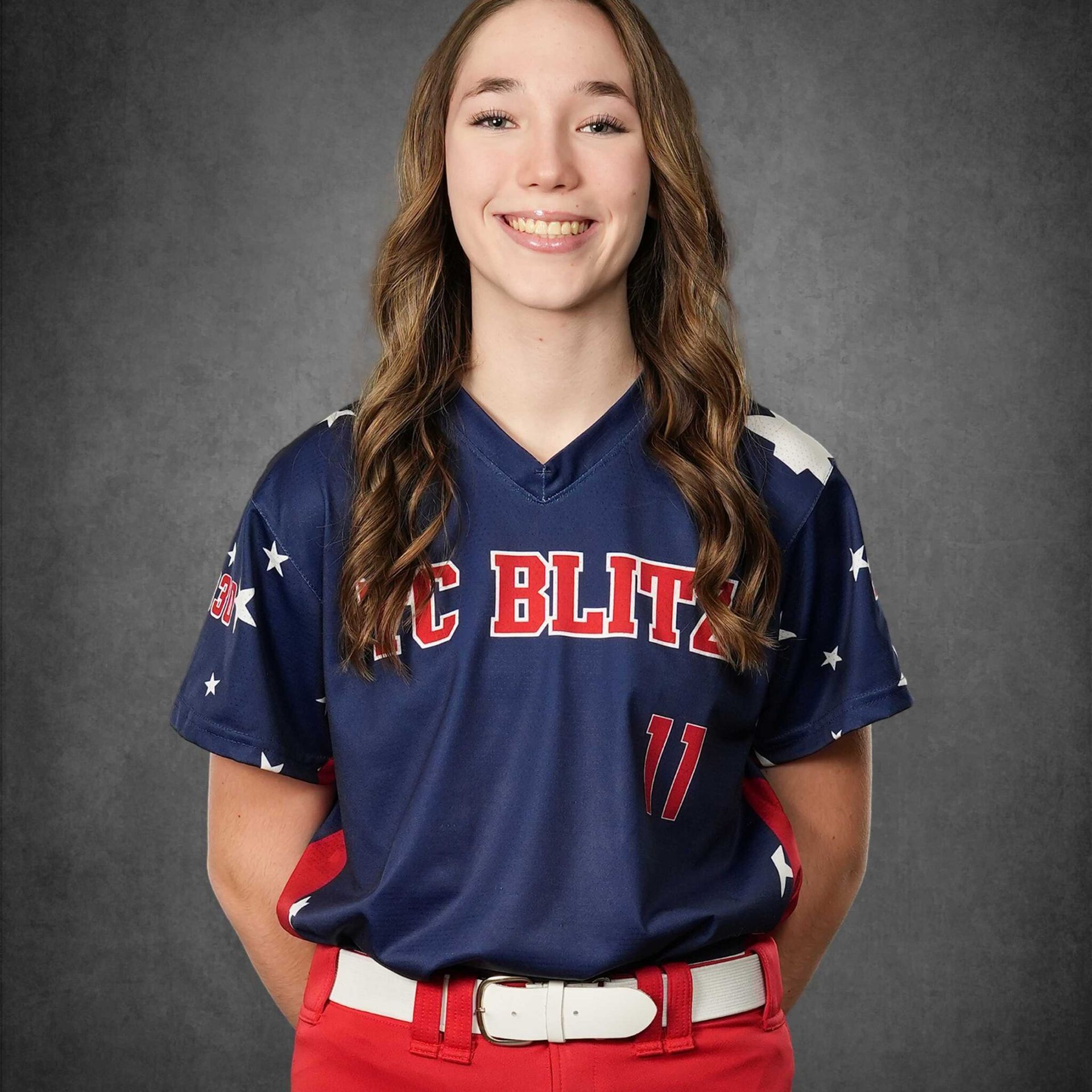 Smiling softball player in blue and red uniform against a gray studio backdrop