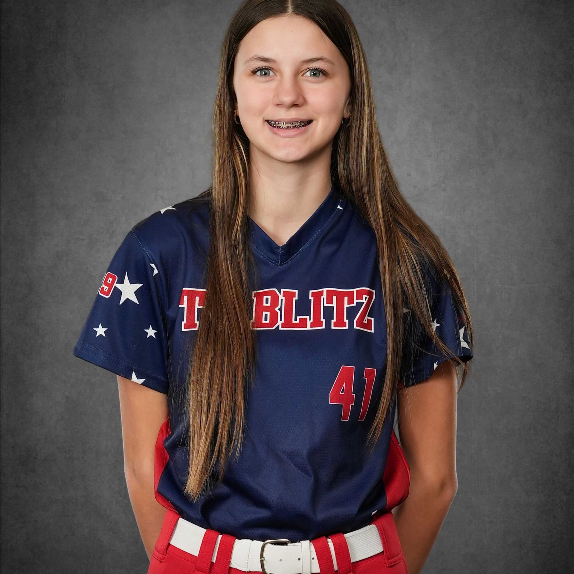 Smiling softball player in navy and red uniform with “T BLITZ” and number 47 against a gray backdrop