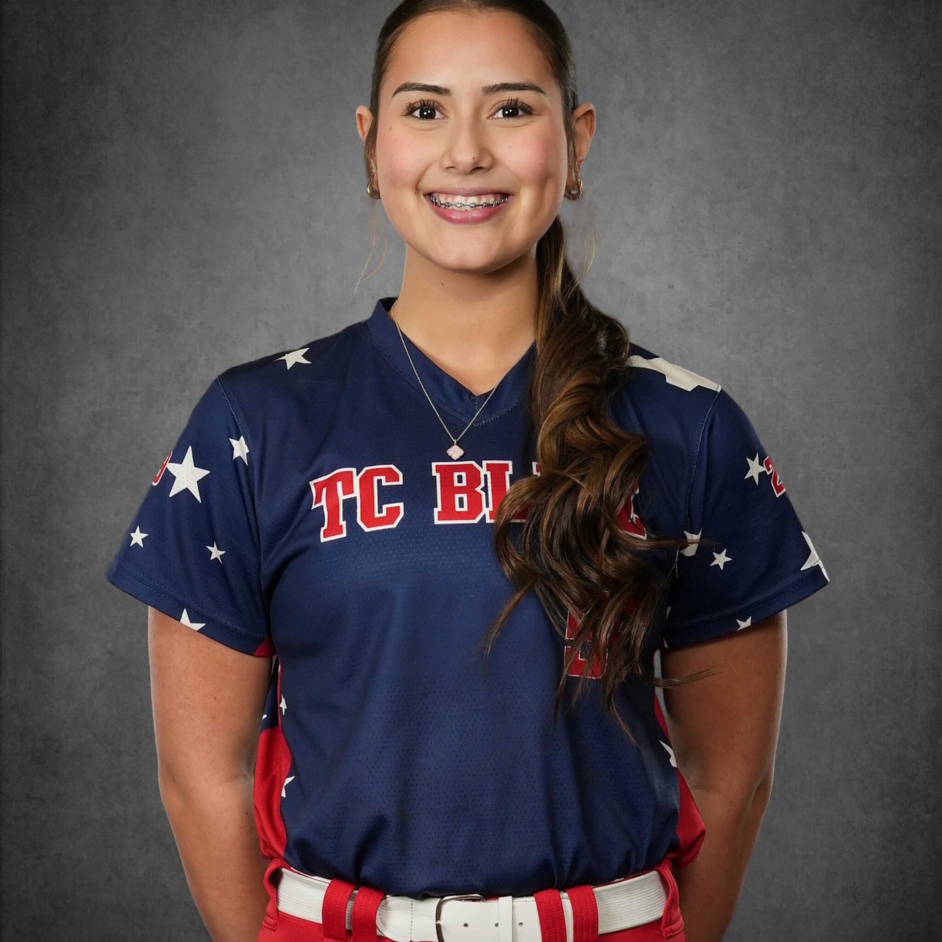 Portrait of a smiling softball player in a navy TC Bats jersey against a gray background