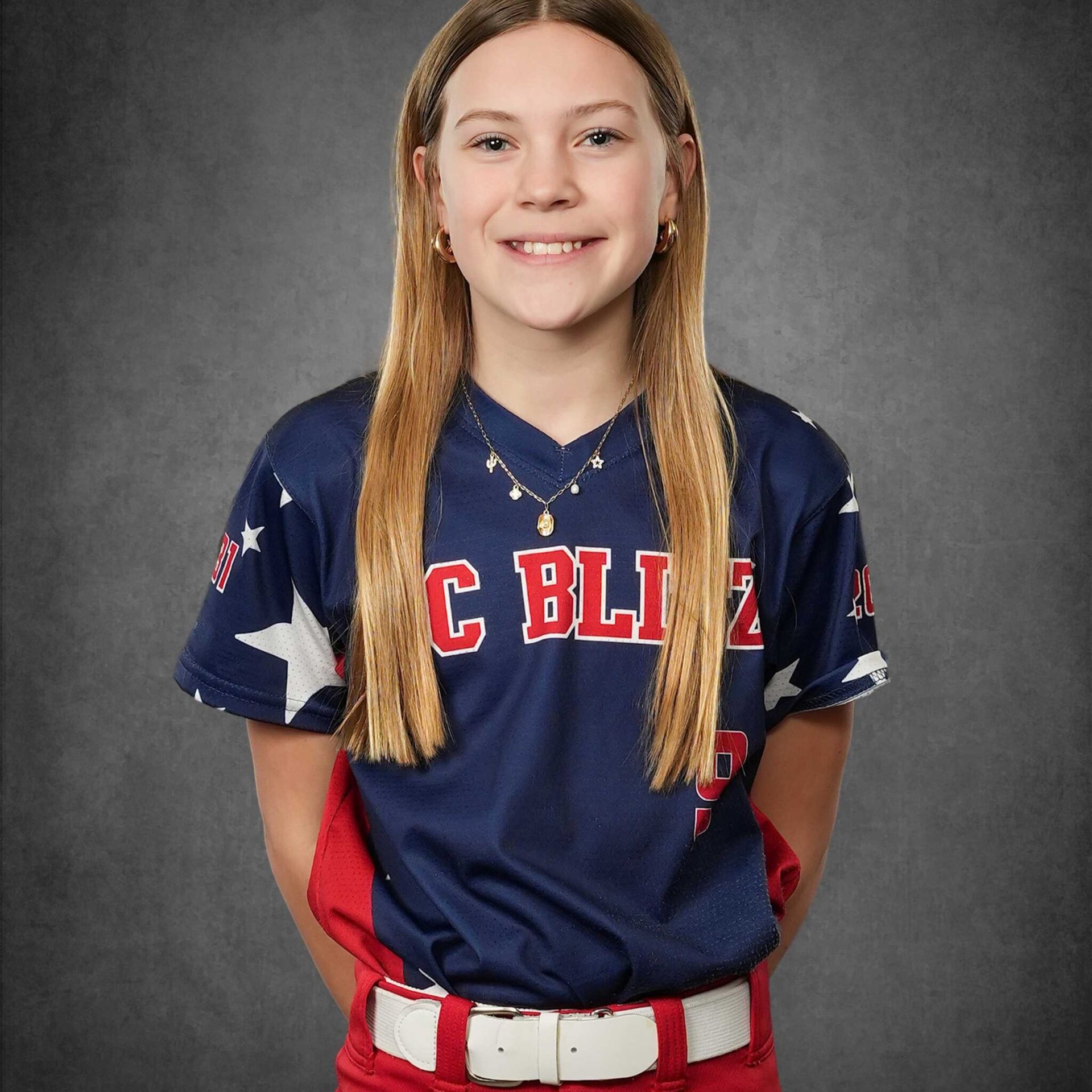 Portrait of a smiling athlete in a navy, red, and white baseball uniform against a gray backdrop
