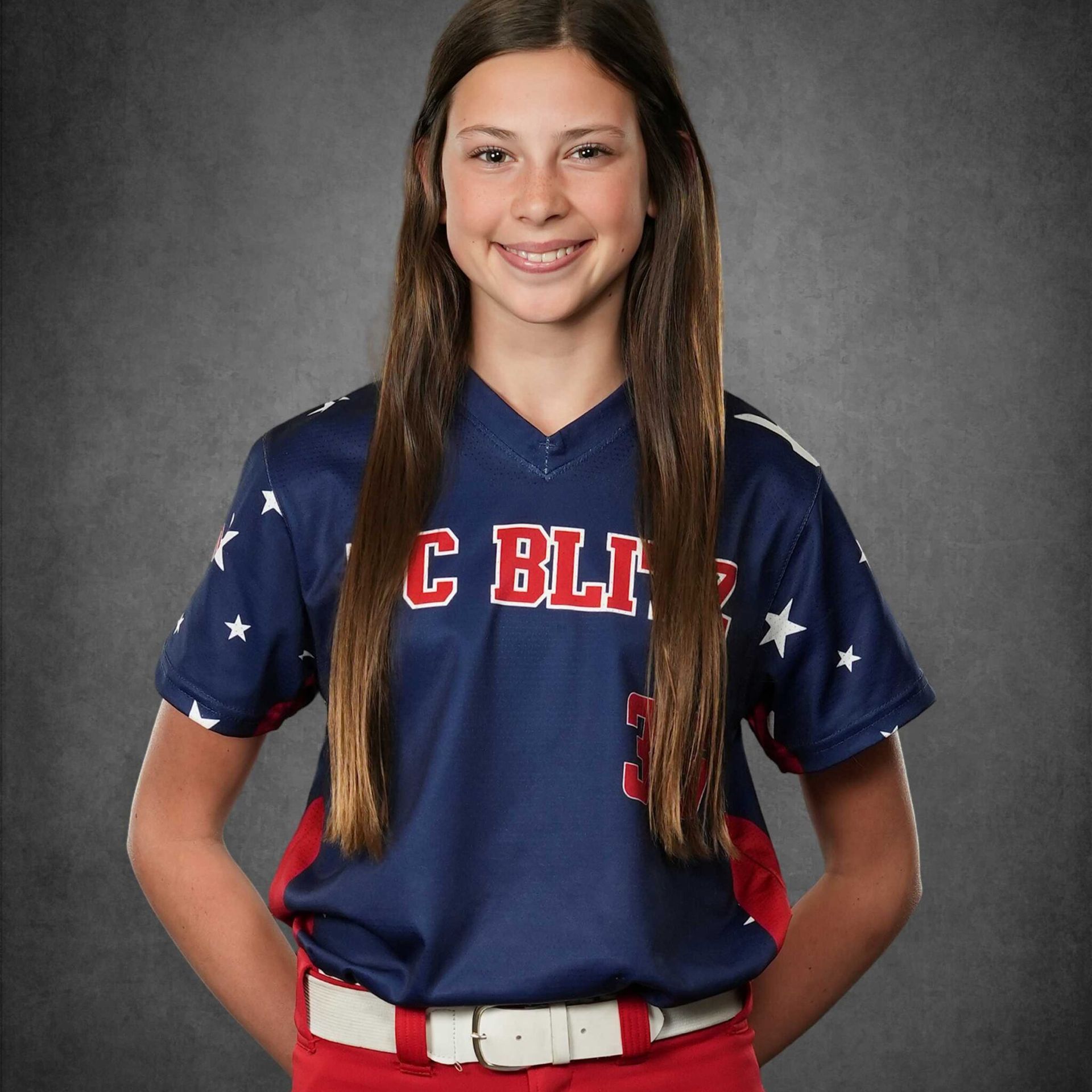 Smiling softball player in navy and red uniform with stars, standing against a gray backdrop