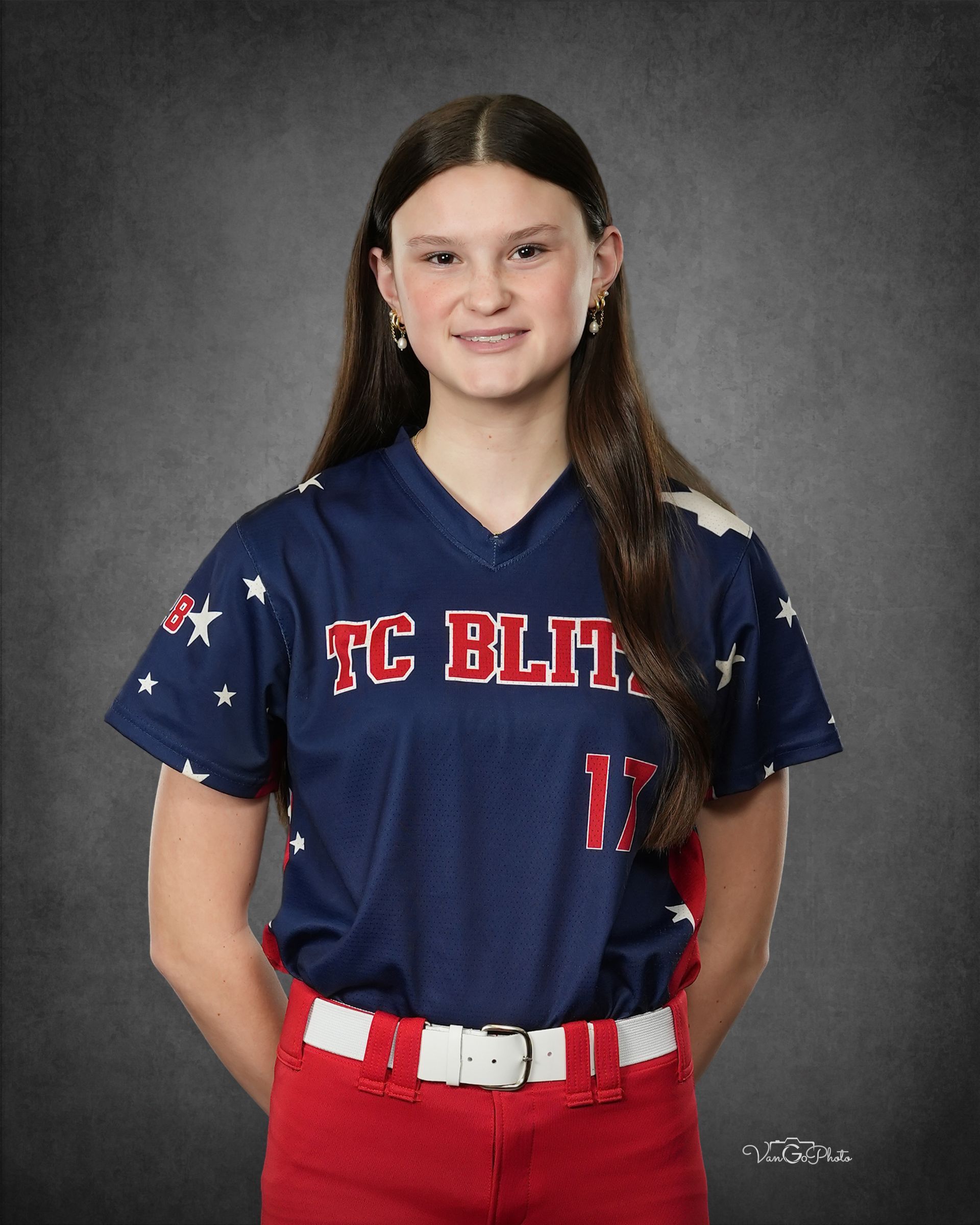 Portrait of a softball player in navy and red uniform, standing against a gray studio backdrop
