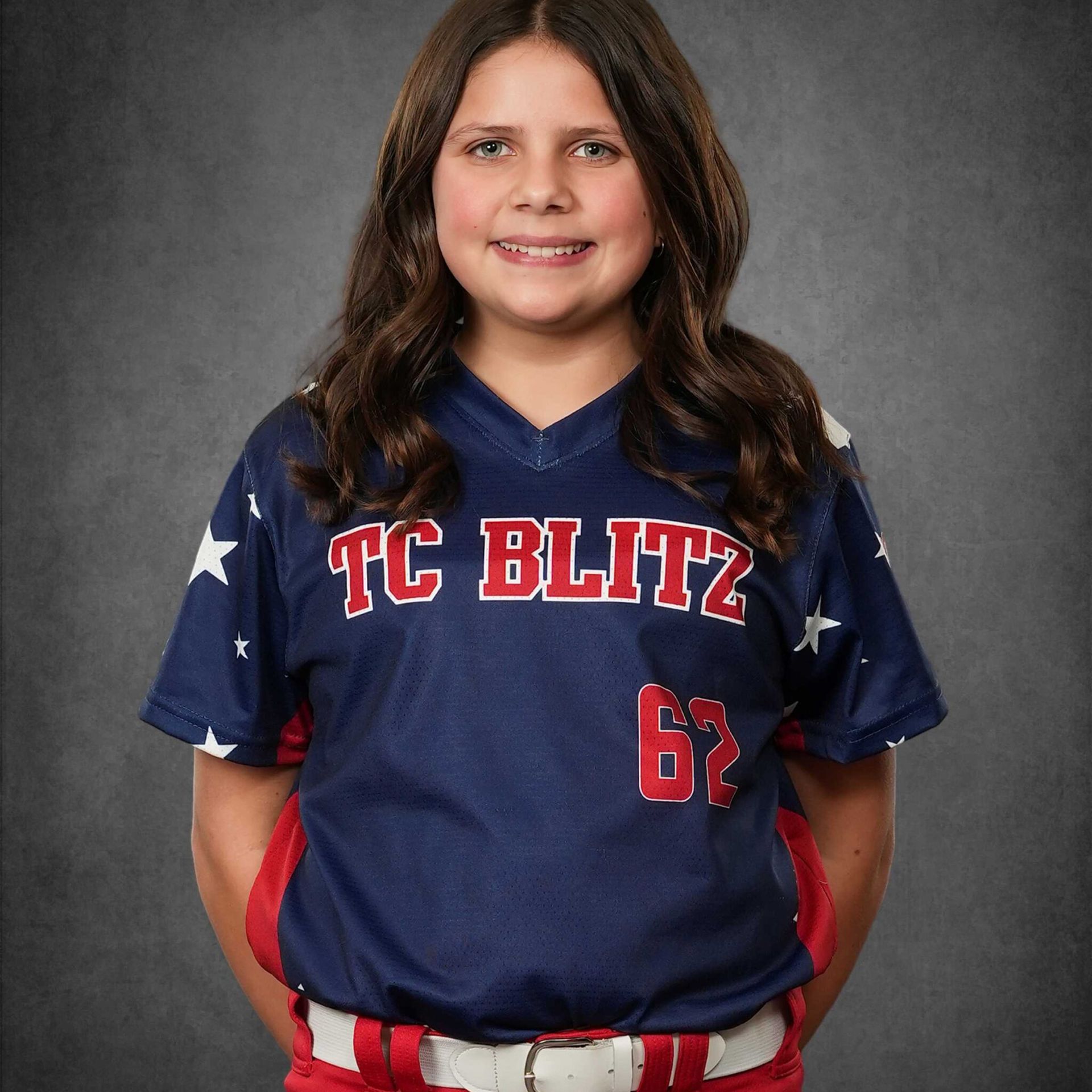 Girl in navy and red TC BLITZ jersey with number 67, standing and smiling against a gray backdrop