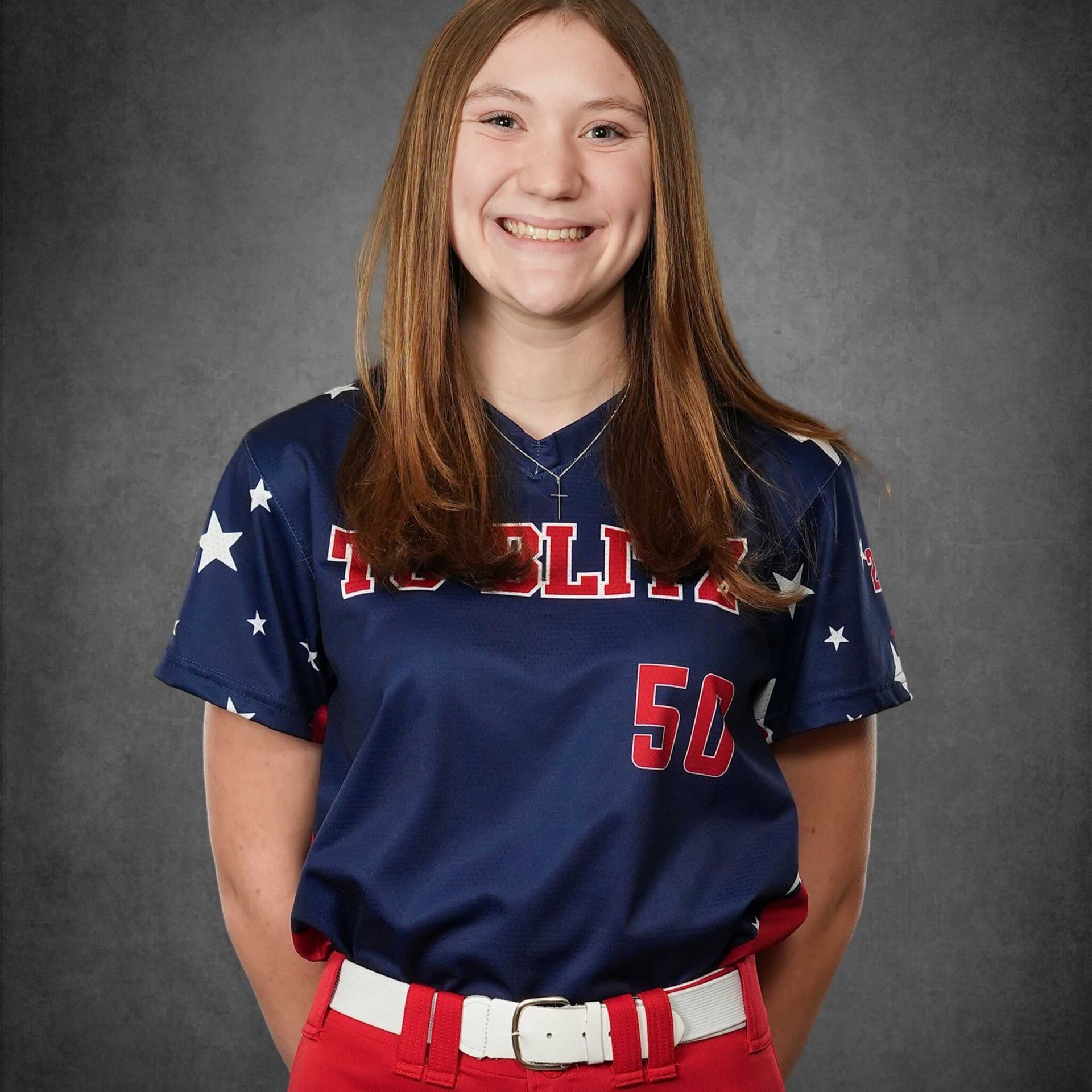 Young athlete in a navy and red softball uniform smiling against a gray studio backdrop