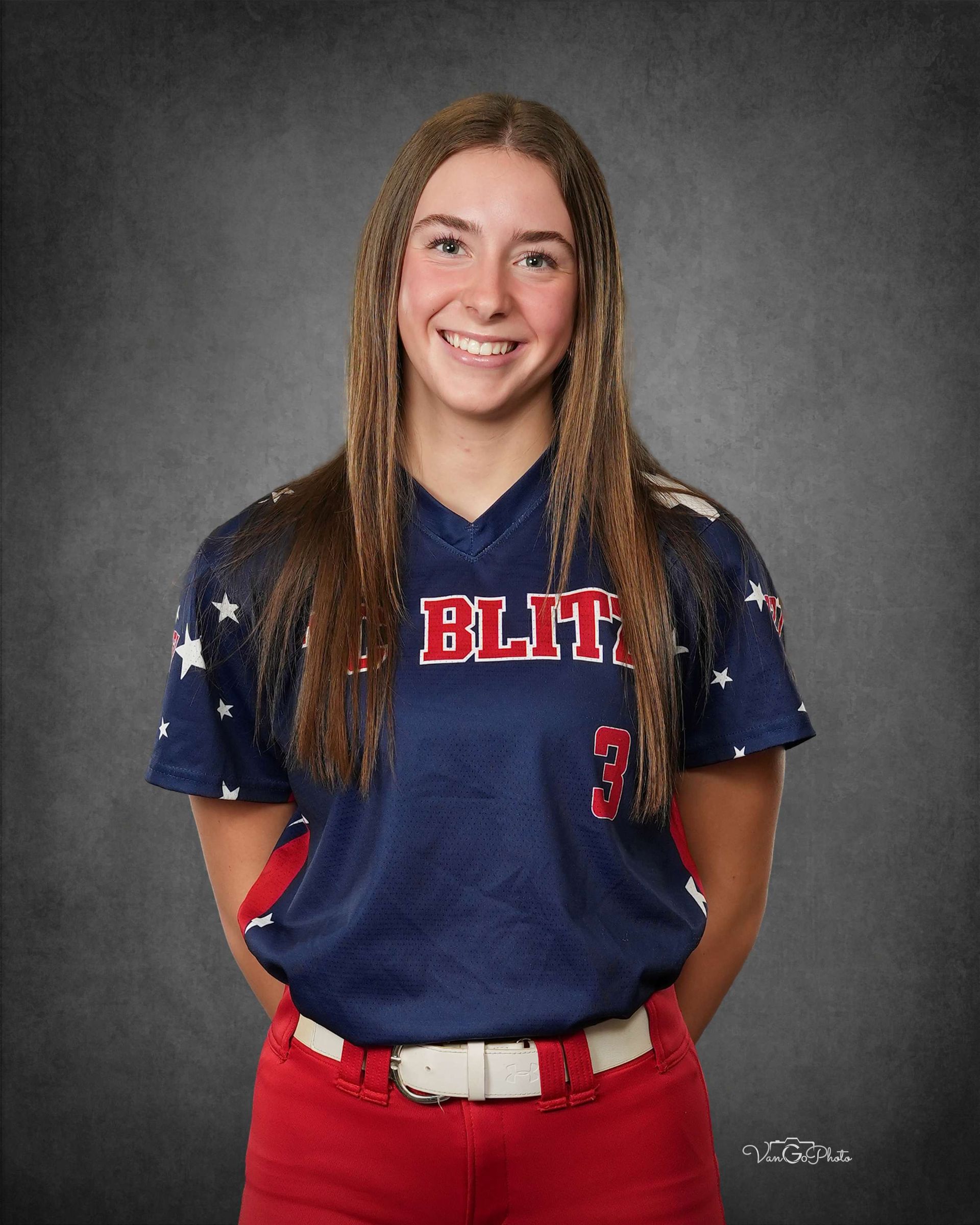 Person in navy sports jersey and red pants, smiling against a gray studio backdrop.