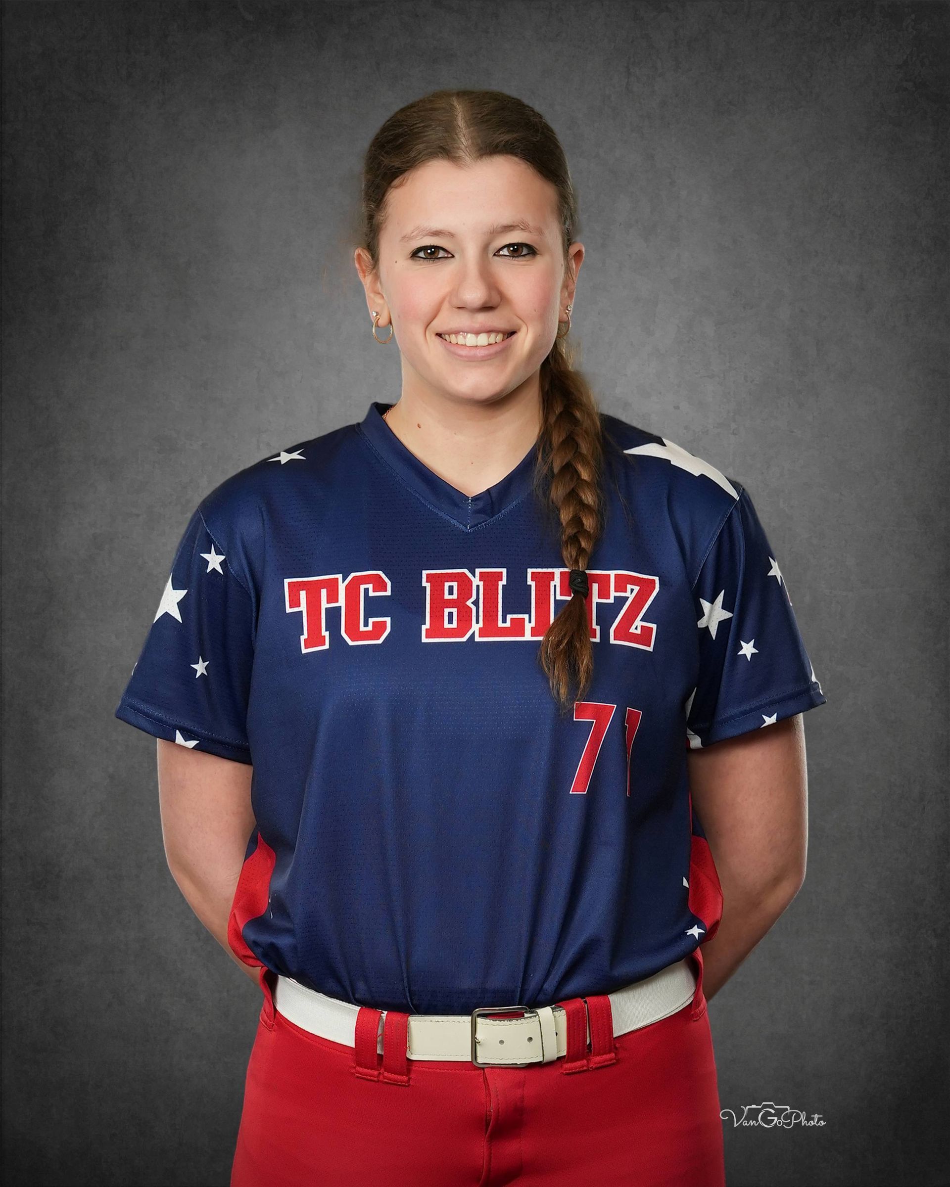 Softball player in navy TC Blitz jersey and red pants, standing against a gray studio backdrop.
