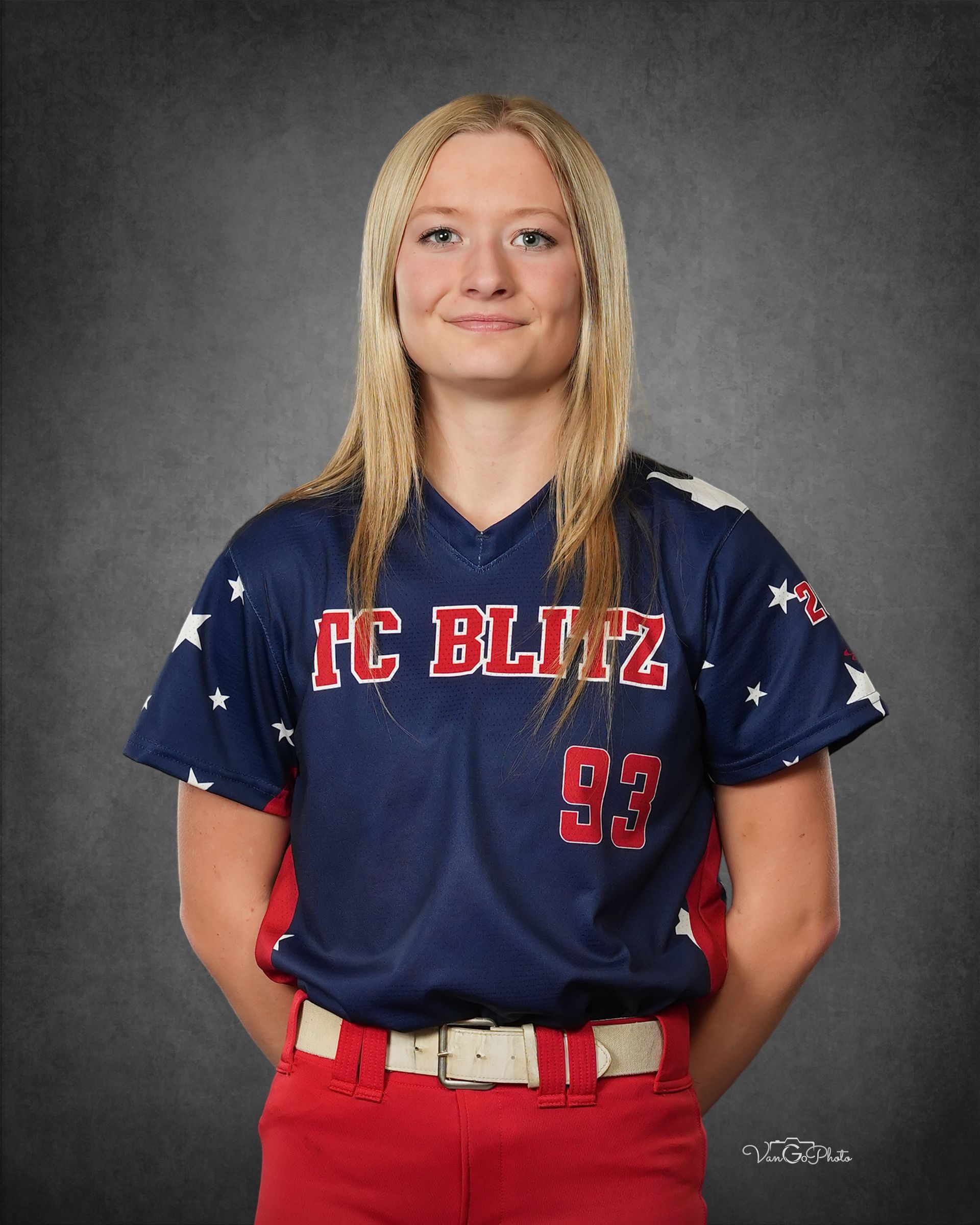 Softball player in navy and red FC Blitz uniform standing against a gray studio backdrop