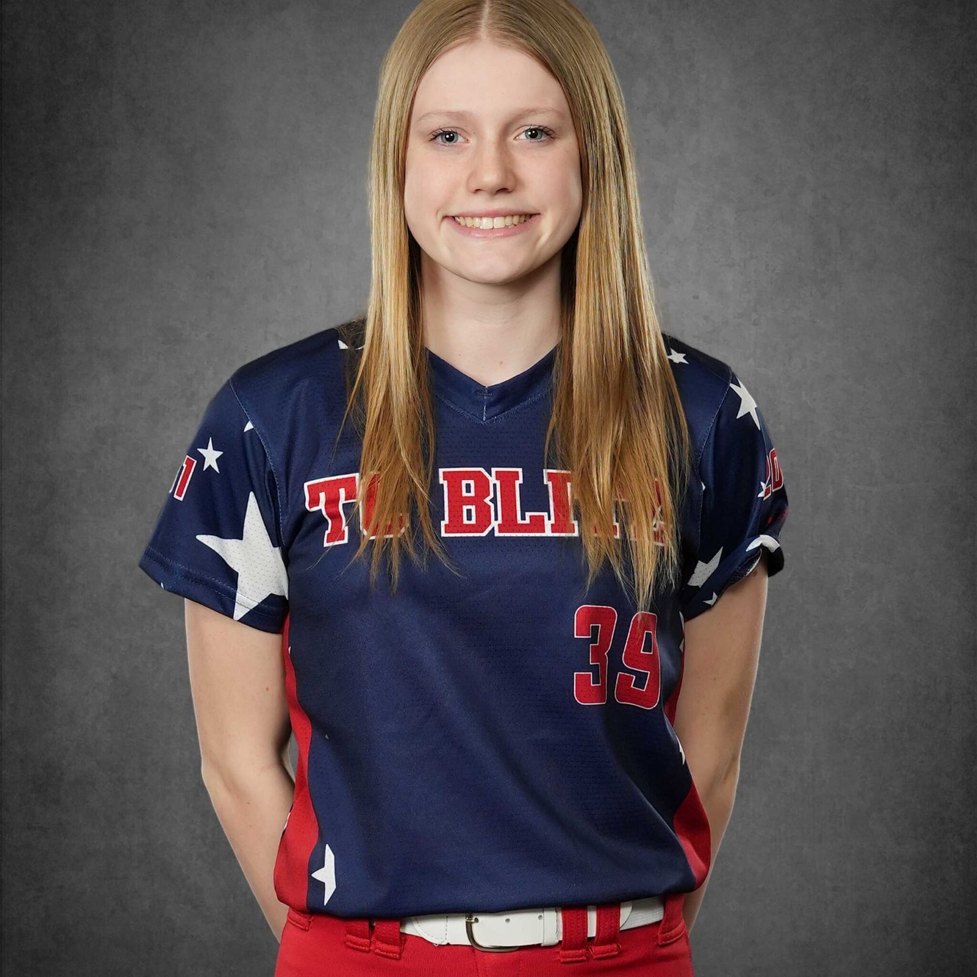 Portrait of a smiling person in a navy and red sports uniform against a gray backdrop