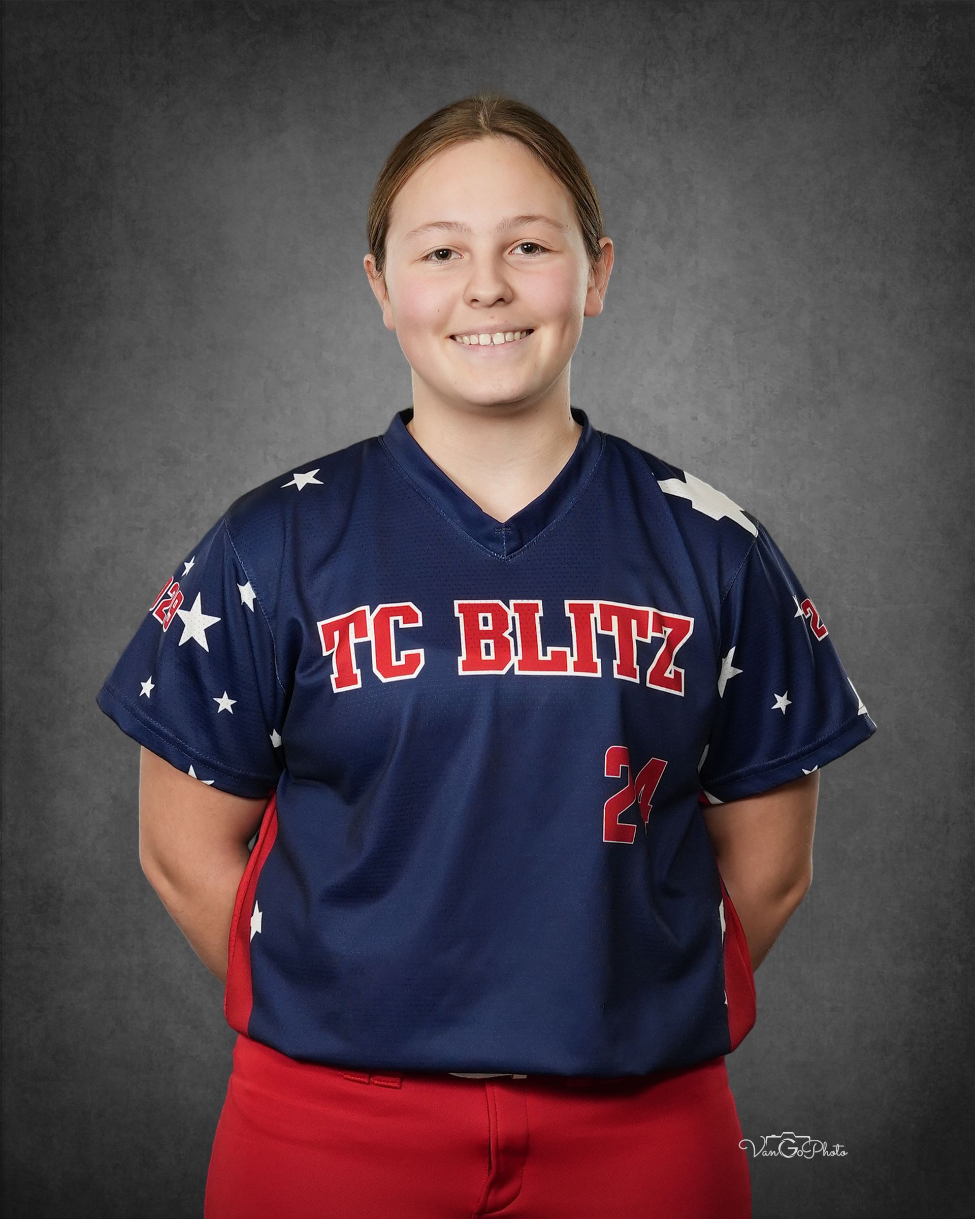 Smiling softball player in navy and red uniform with “TC BLITZ” standing against a gray studio backdrop