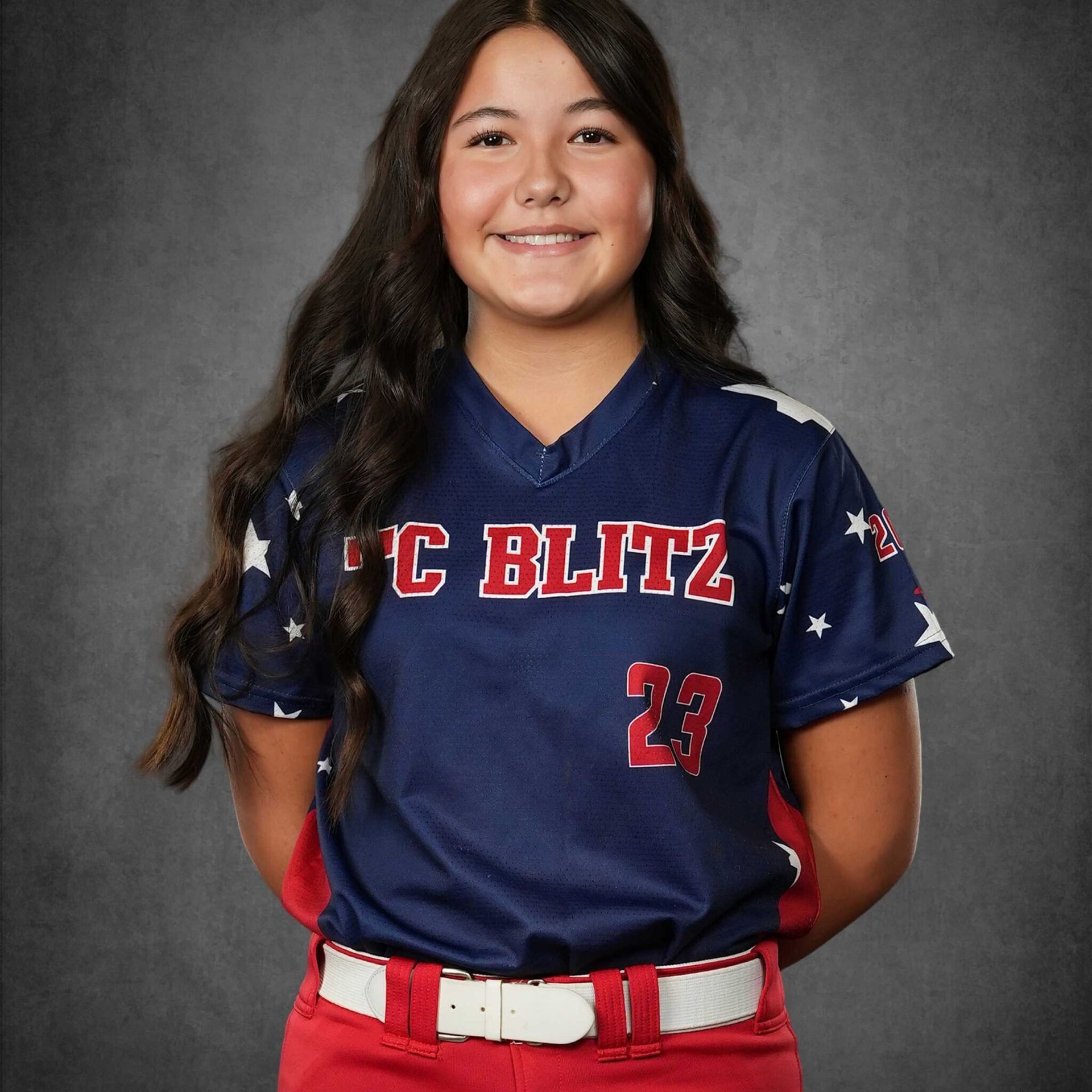 Portrait of a smiling softball player in a navy and red uniform against a gray studio backdrop