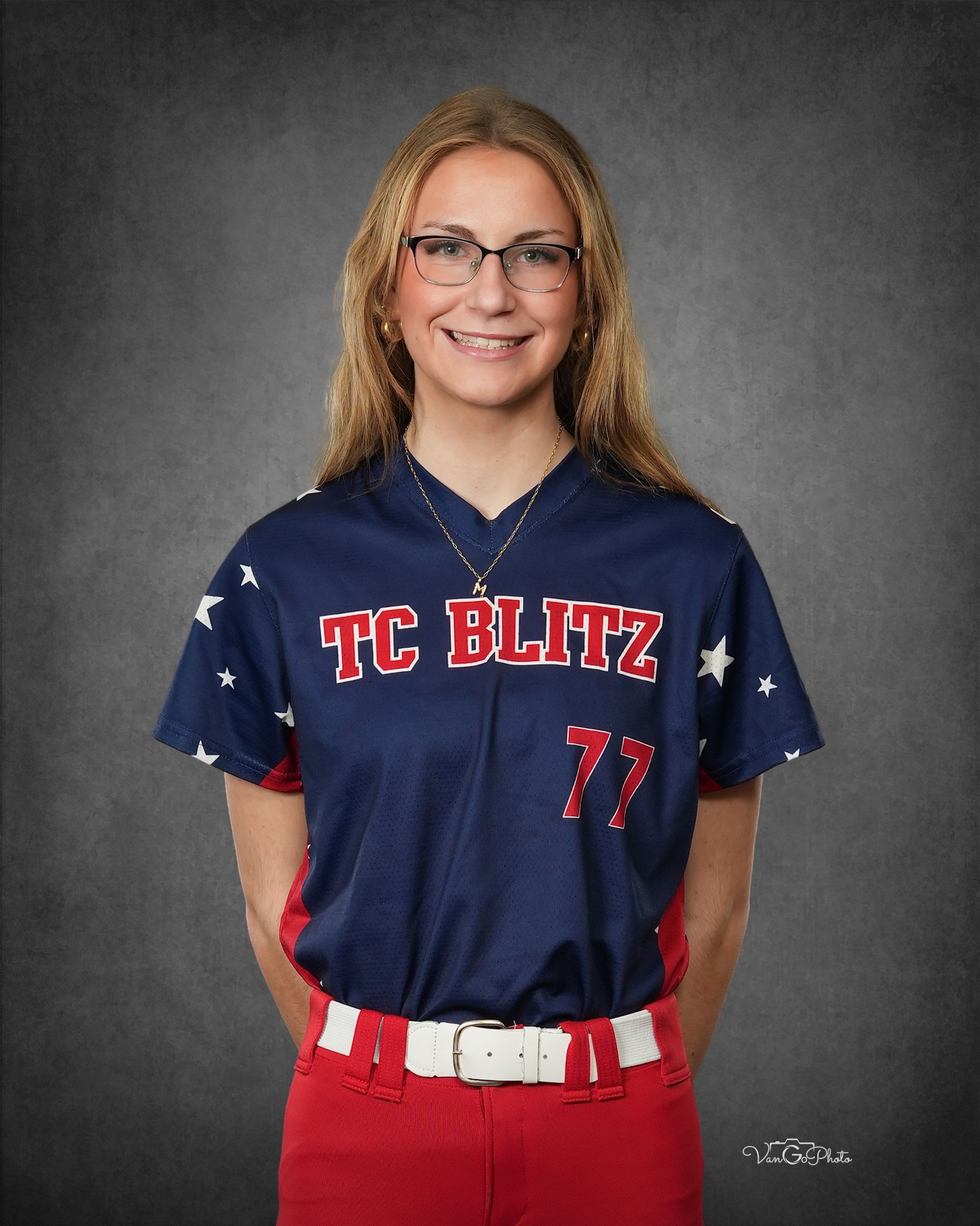 Studio portrait of a smiling athlete in a navy TC BLITZ jersey and red pants, wearing glasses.