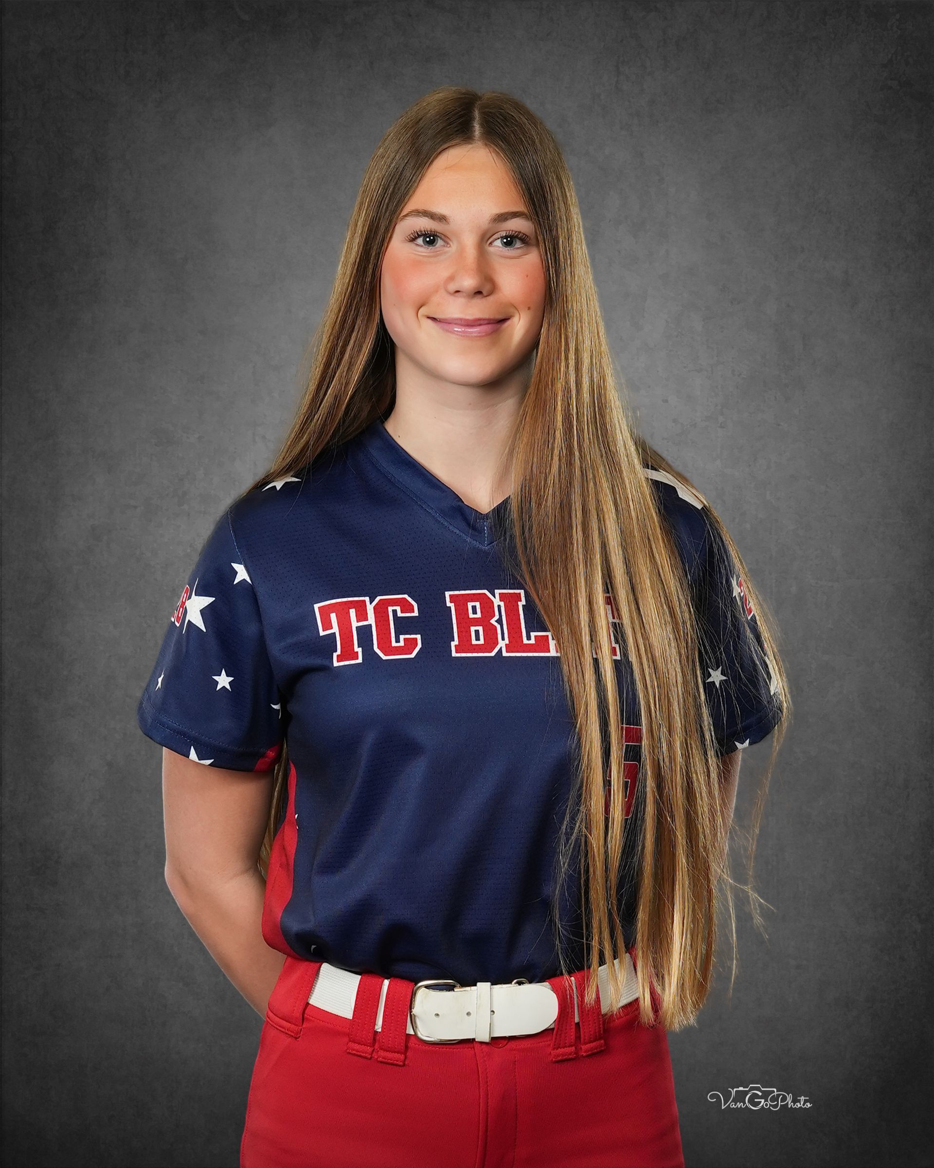 Portrait of a smiling person in a navy jersey and red pants against a gray studio backdrop